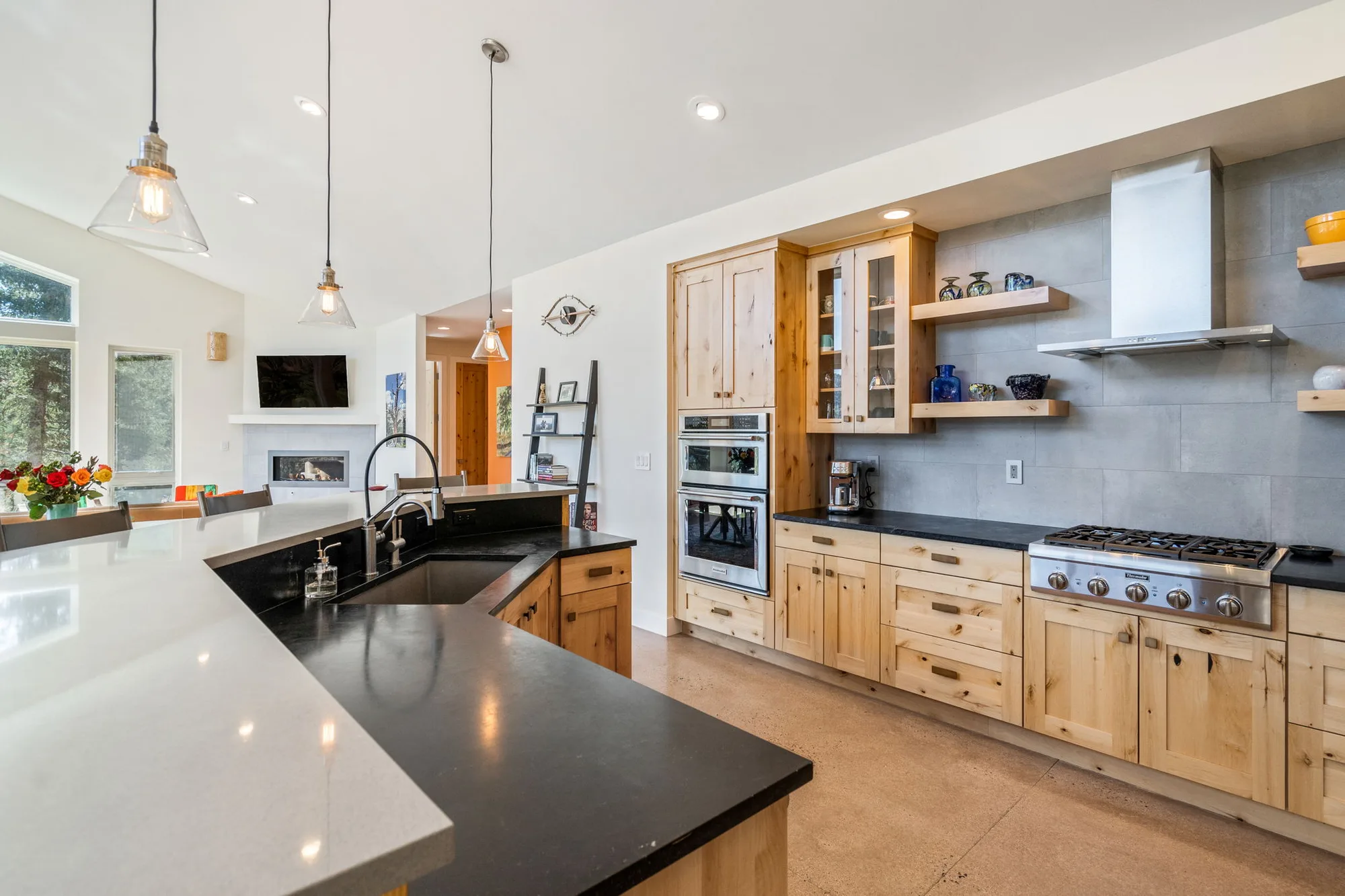 Kitchen counters in honed black granite and white quartz, with a gas cooktop and floating alder shelves