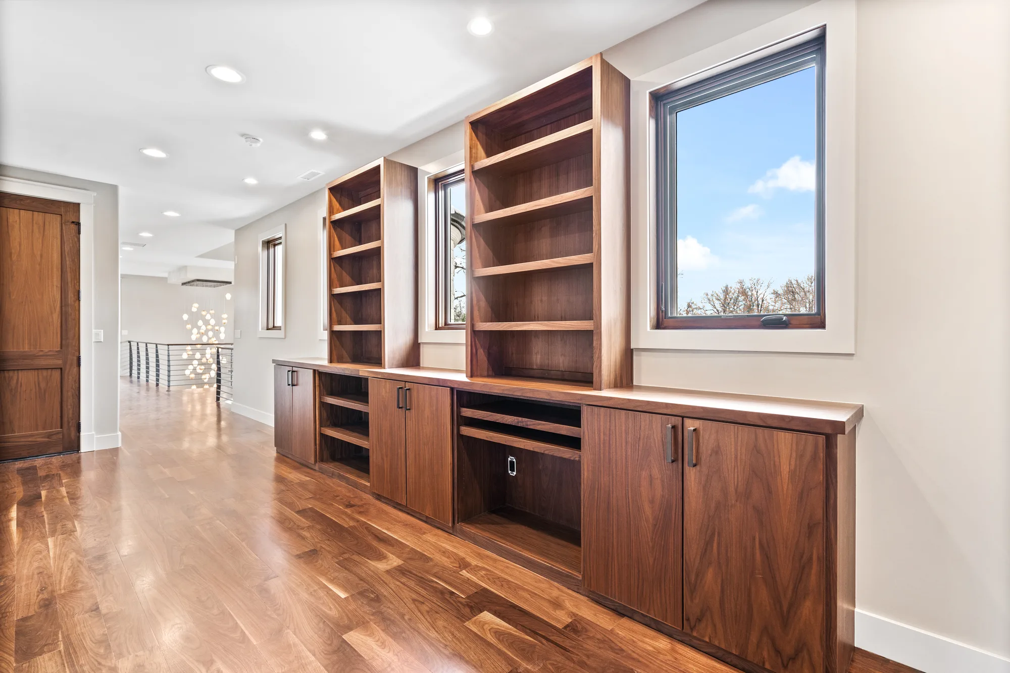 Upper hall lined with walnut built-in cabinetry and open shelving between windows, looking back to the stair