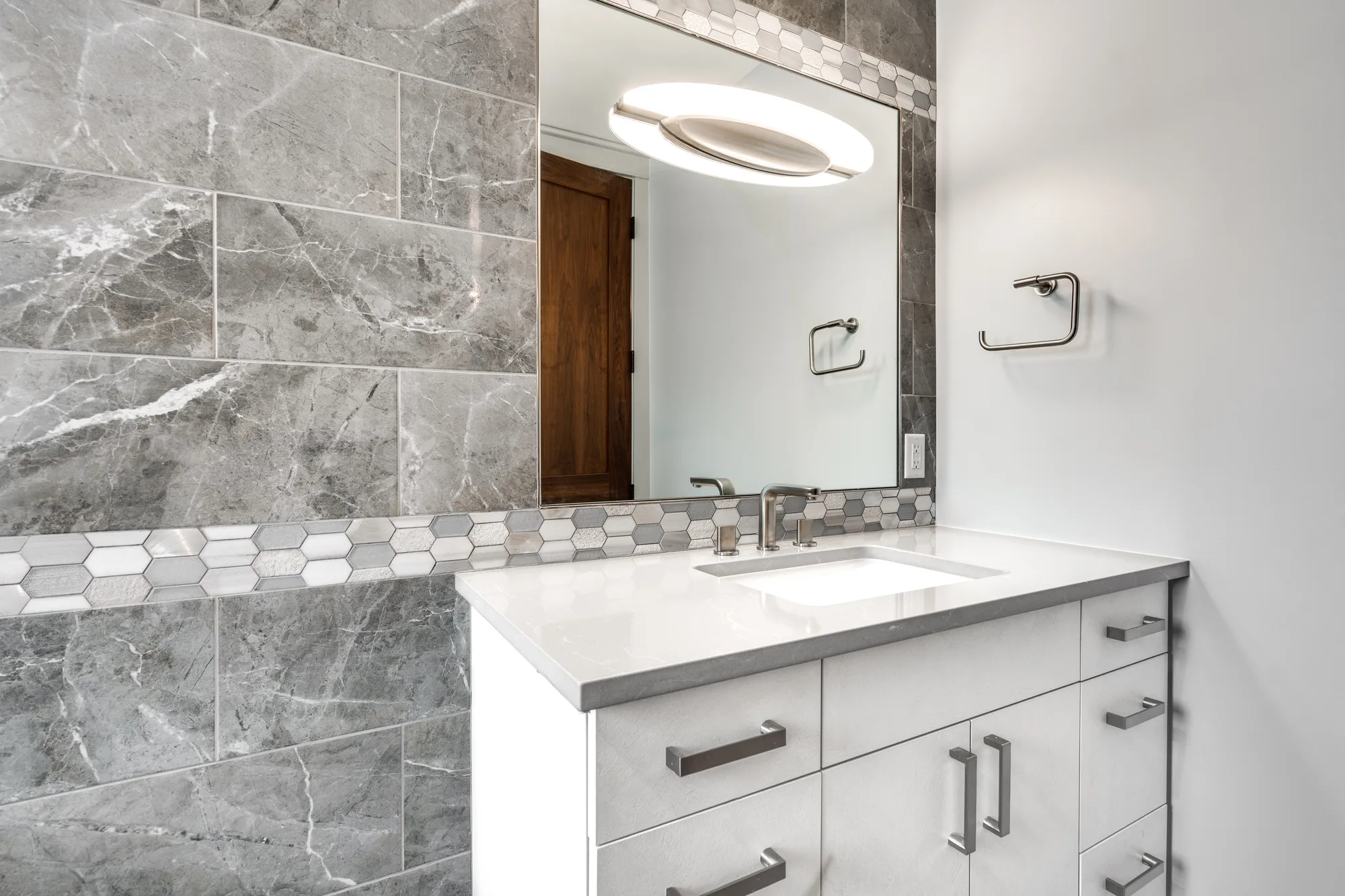Guest bath vanity with grey marble tile, a hexagon mosaic band, and a quartz counter under a frameless mirror