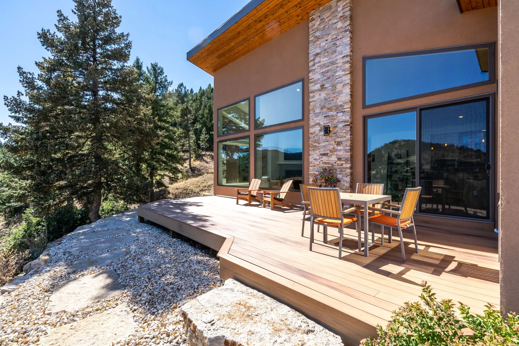 The deck seen from below, with a stacked-stone column, deep cedar soffit, and full-height glass