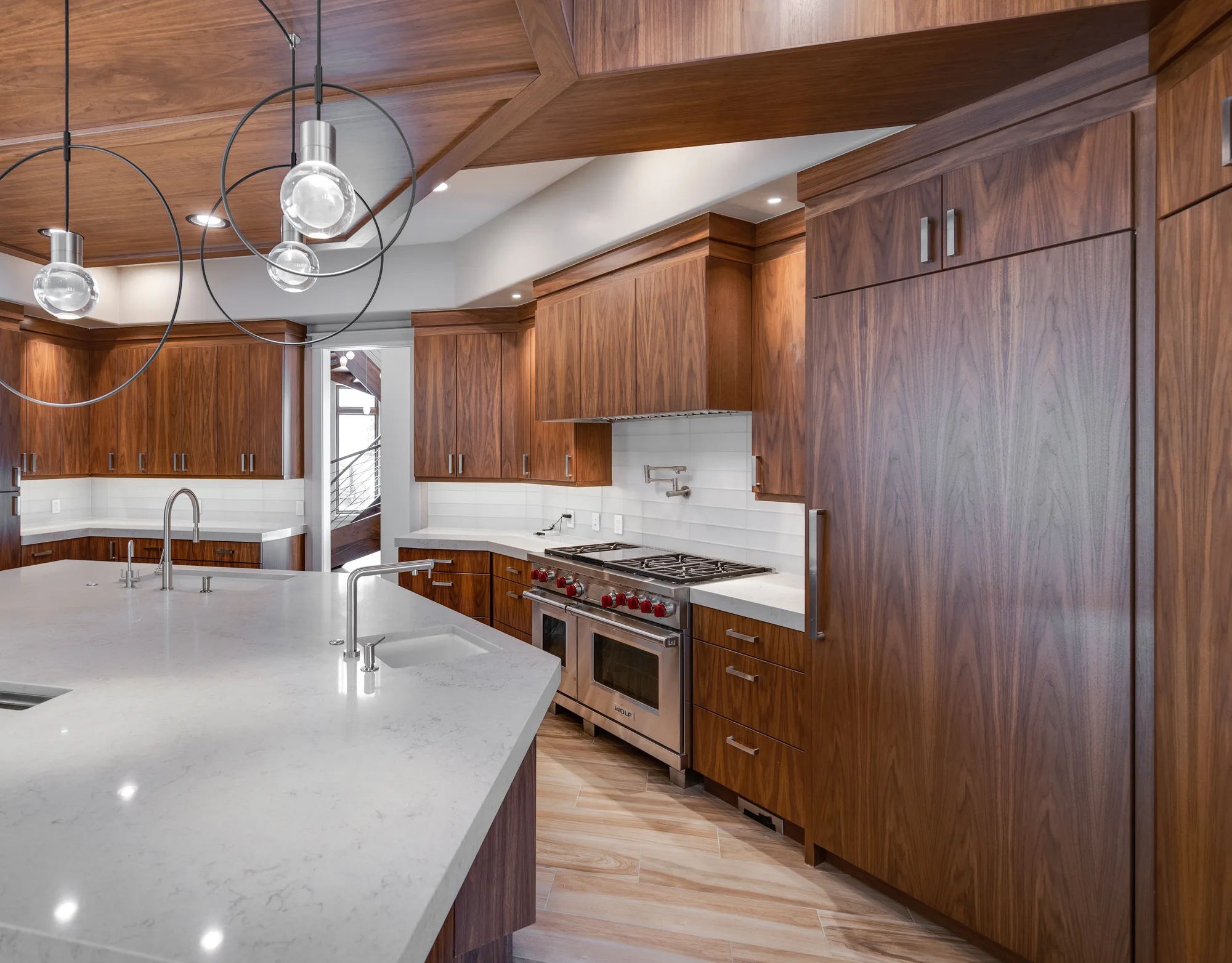 Kitchen range wall in walnut with a white tile backsplash, pot filler, and sculptural ring pendants above the island