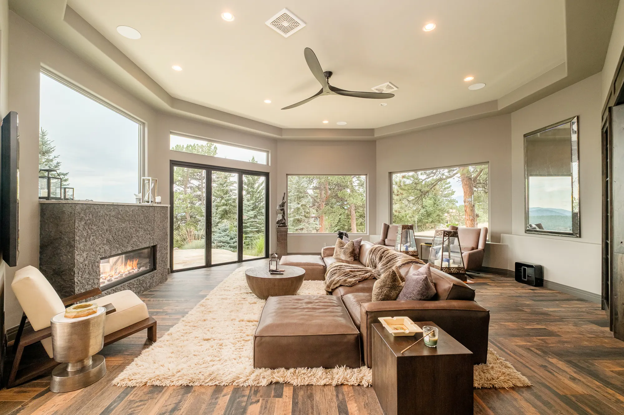Family room with a linear stone fireplace, leather sectional and glass doors to the terrace.