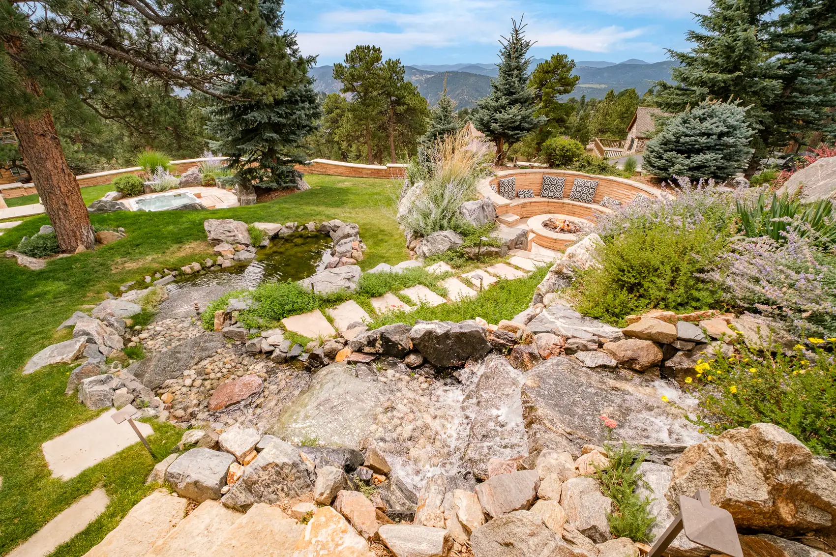 Flagstone steps threading a rock garden past a pond toward a sunken fire pit.