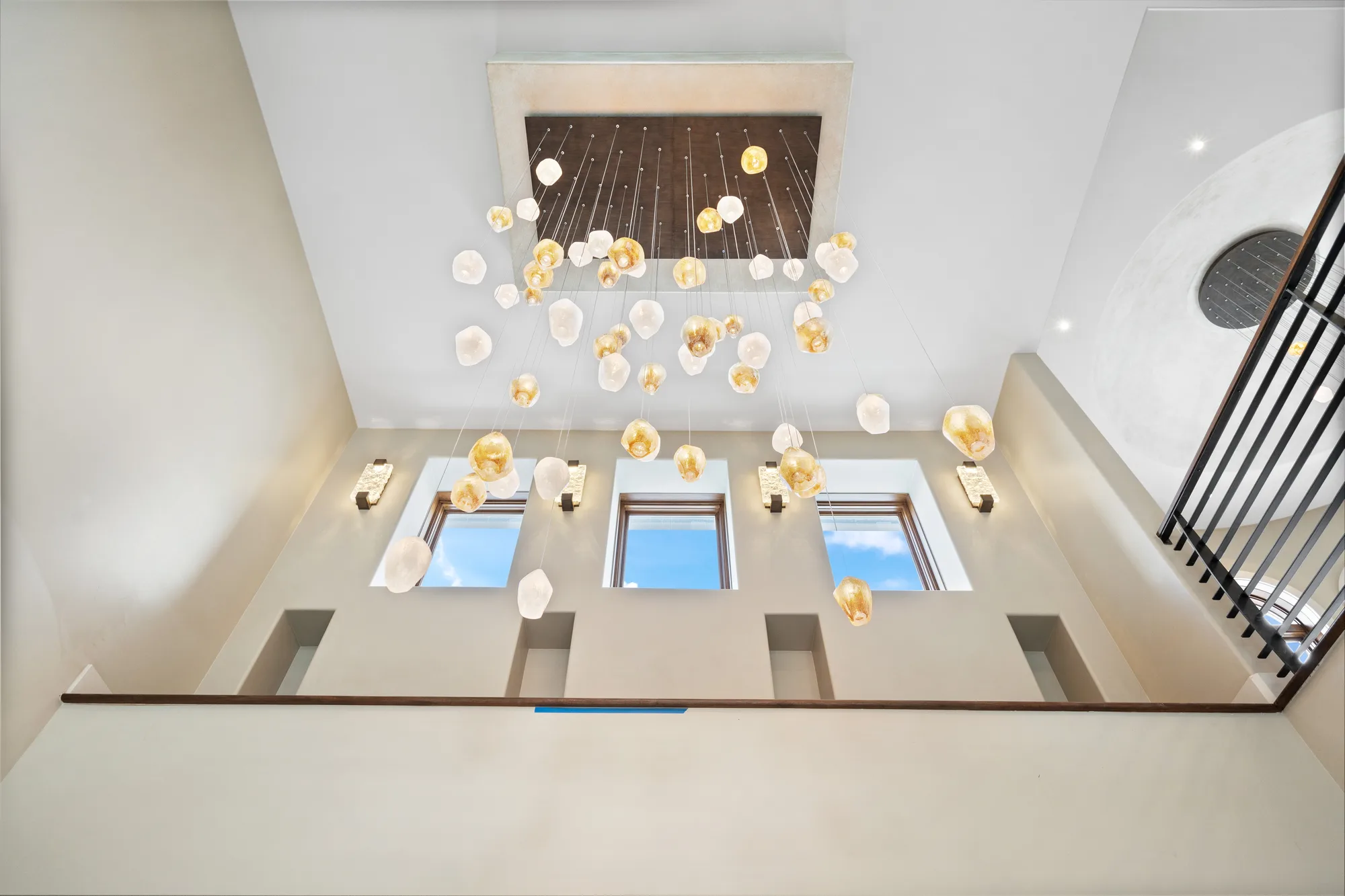 The pendant cascade seen from the upper landing, dozens of alabaster and amber glass forms suspended on wires from a bronze canopy