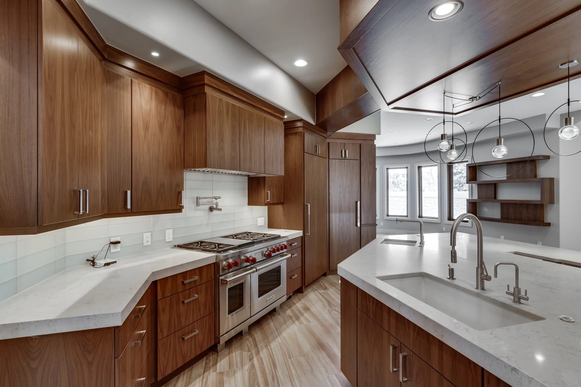 Wide view of the kitchen showing the full run of walnut cabinetry, twin sinks, and the faceted ceiling detail