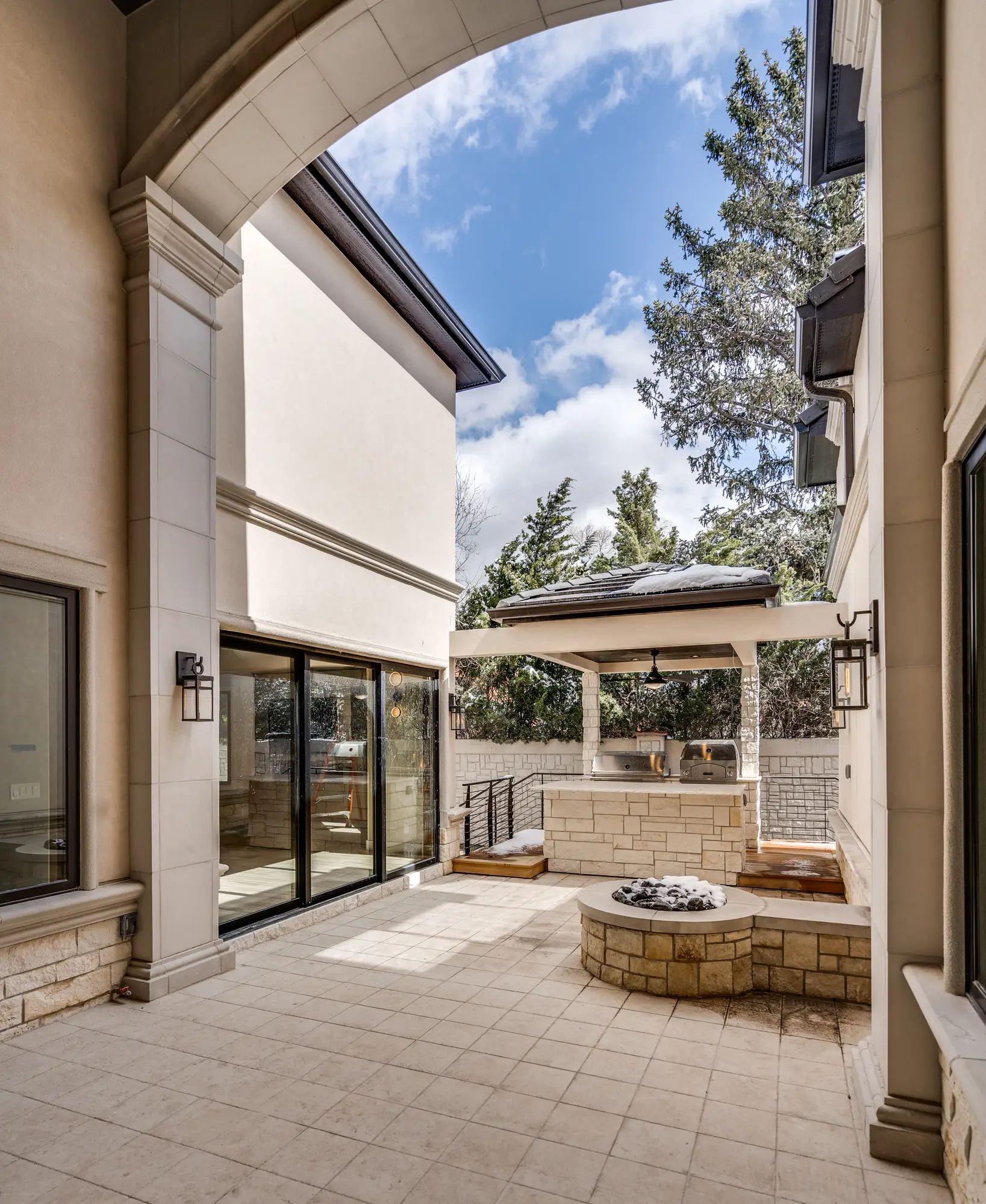 Cast stone loggia arch opening onto a courtyard with a stone fire pit, seat wall, and covered outdoor kitchen