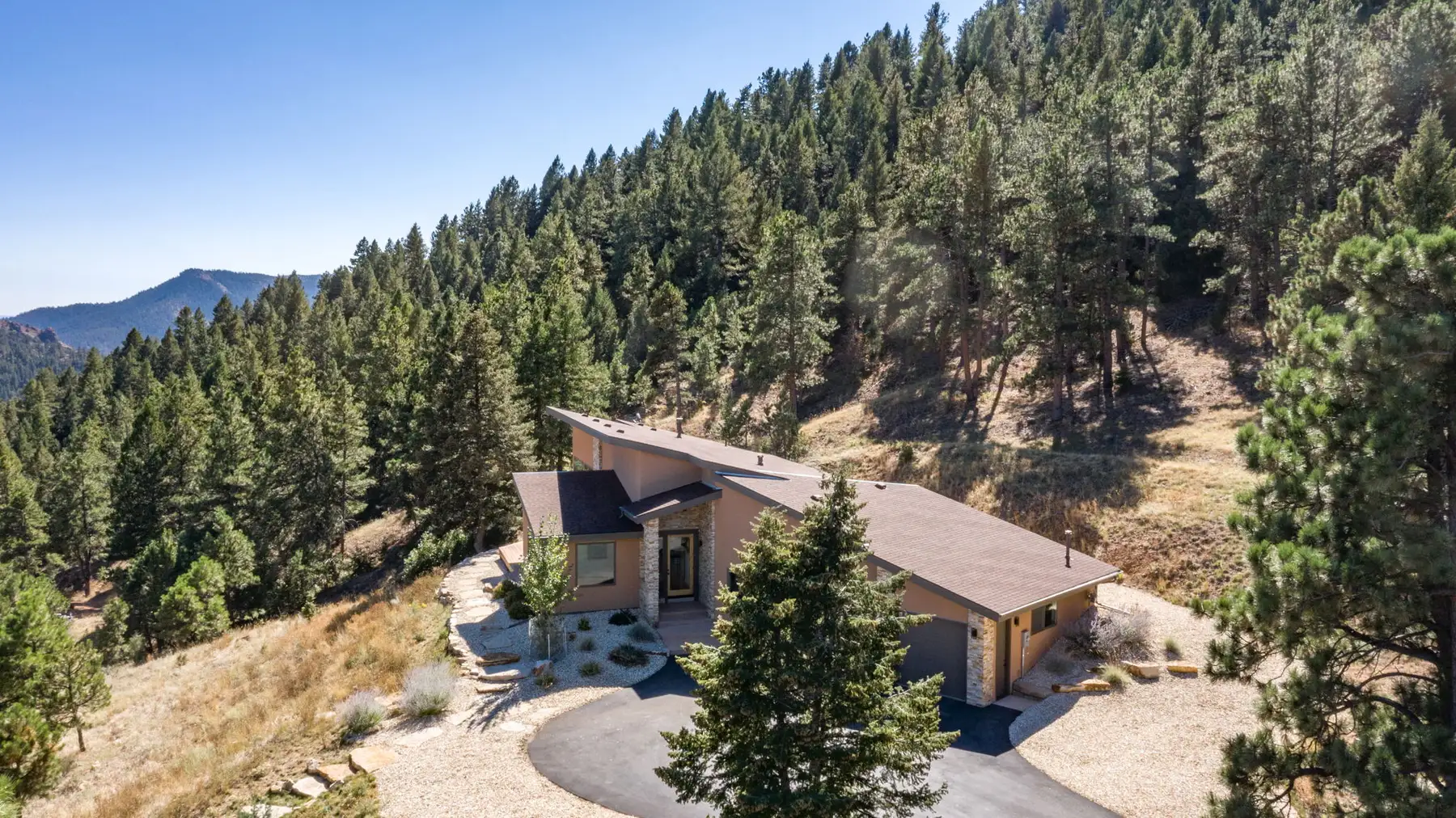 Aerial view of the house and its curved drive tucked into the ponderosa on a steep forested slope