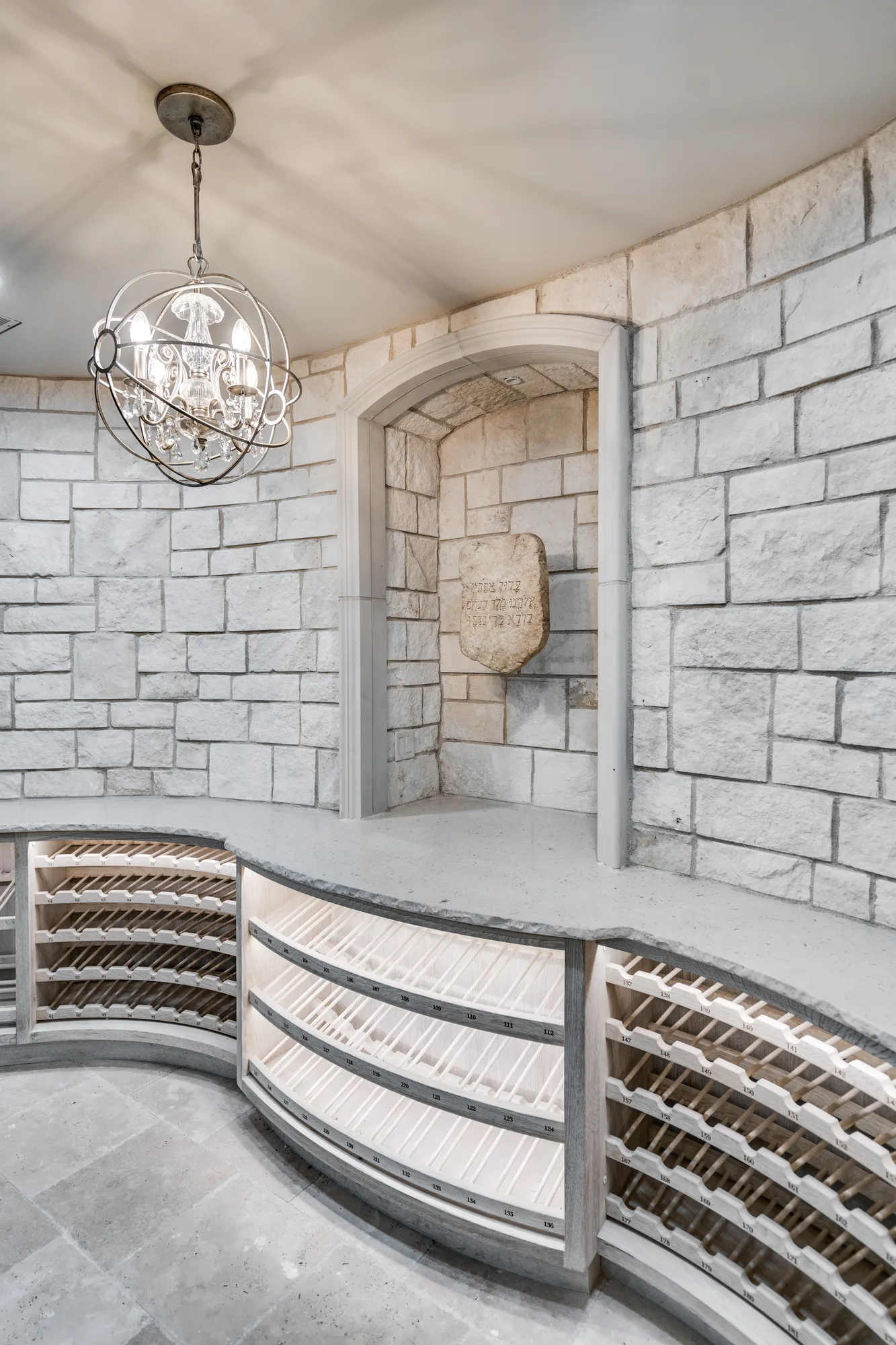 Wine room detail — curved racking meeting the cut stone wall beneath a stone counter