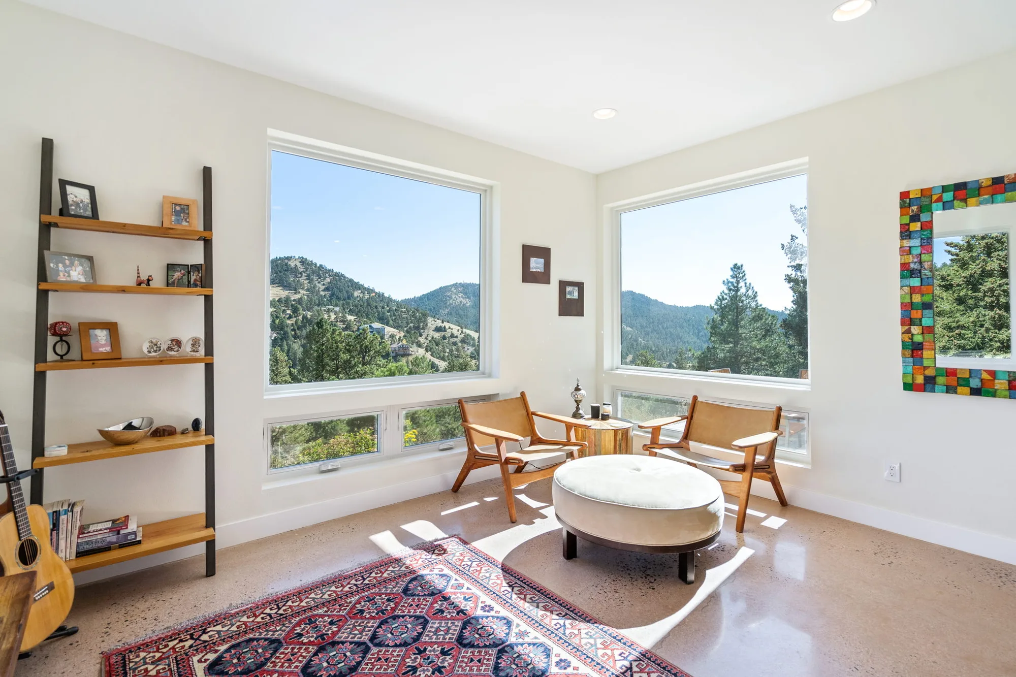 Corner sitting room with two large windows onto the ridgeline, leather chairs, and a polished concrete floor