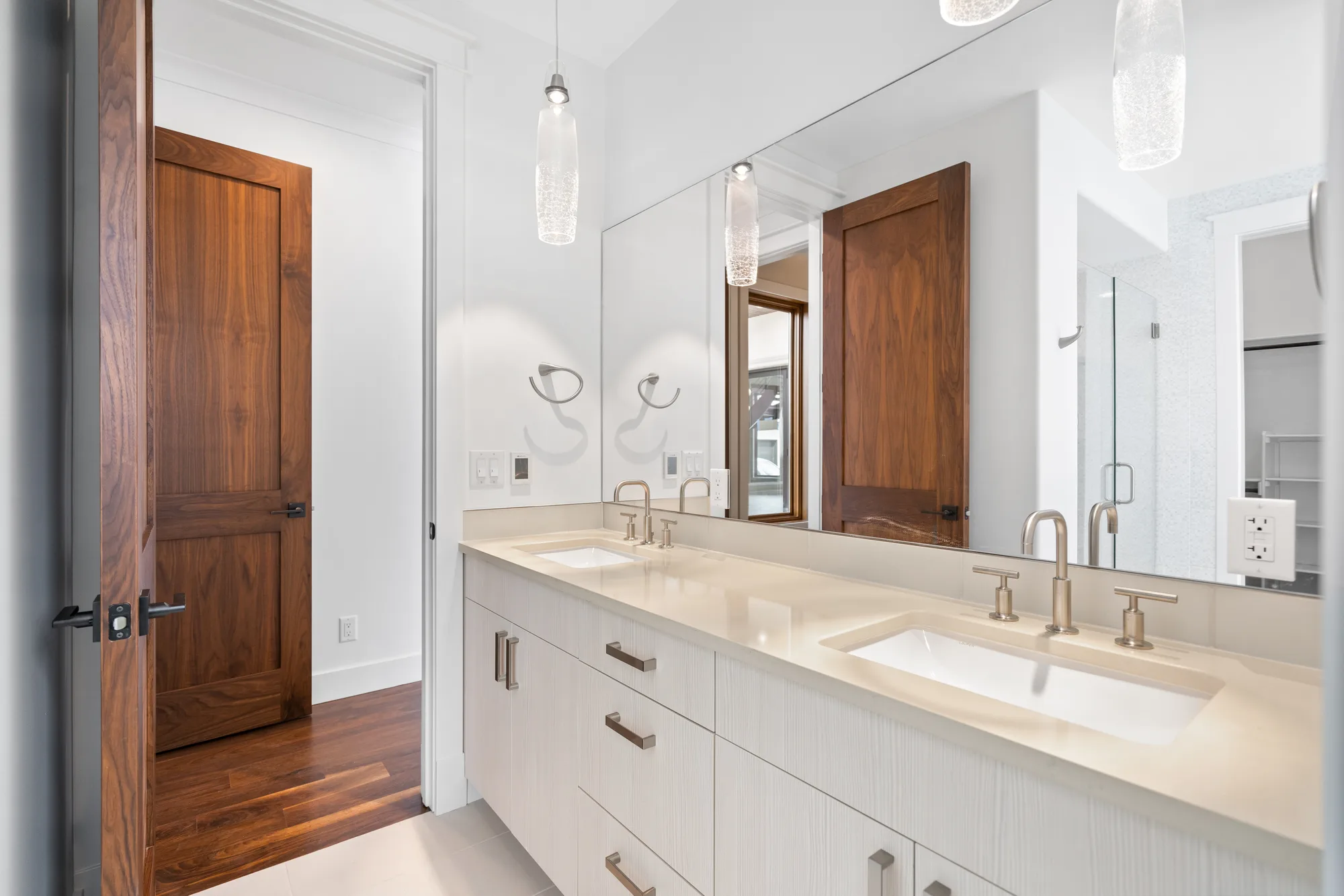 Bath with a double vanity in textured white cabinetry, quartz counter, and a walnut door
