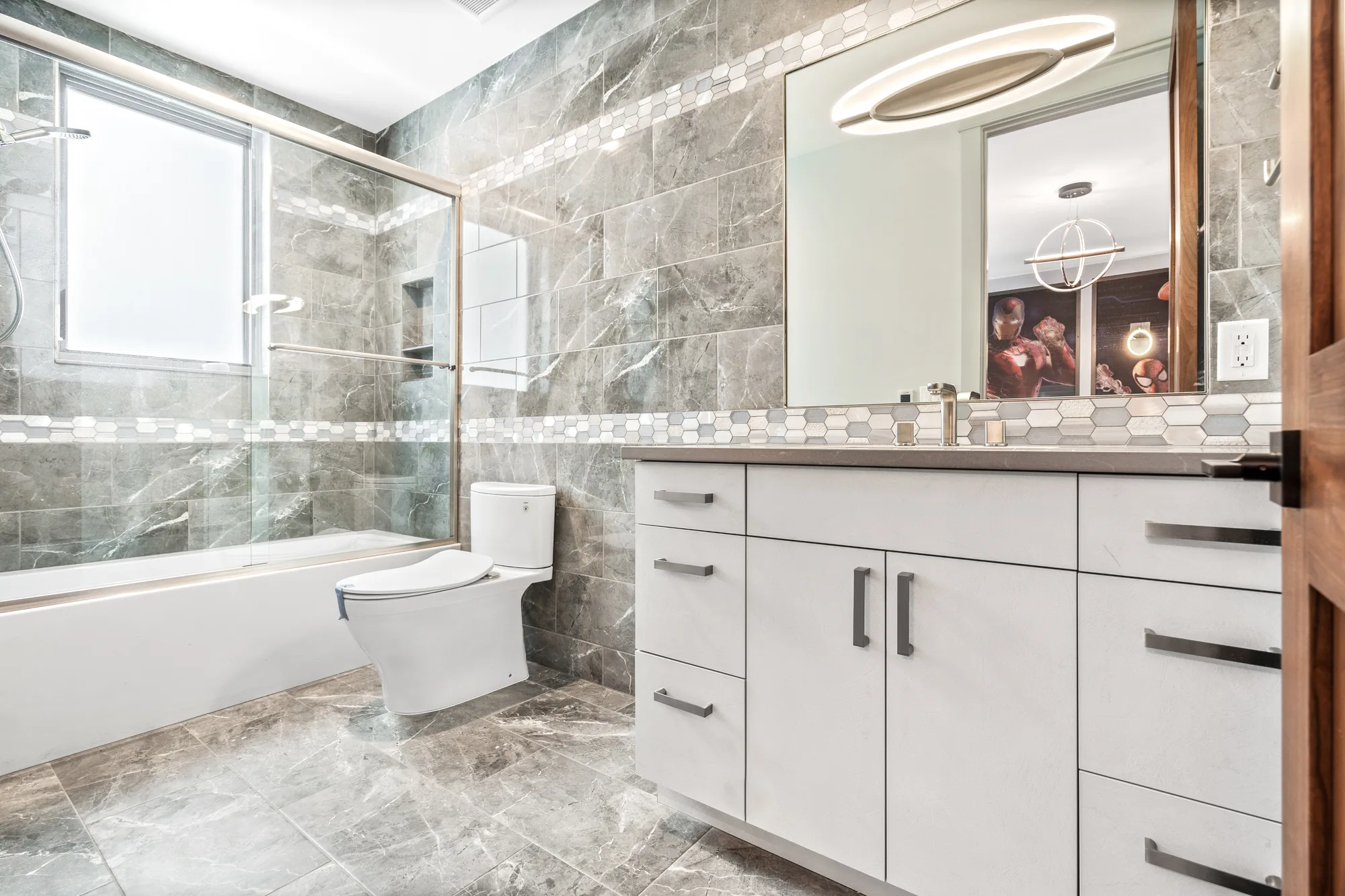 Guest bath with a glass-enclosed tub and shower in grey marble tile beside a long white vanity