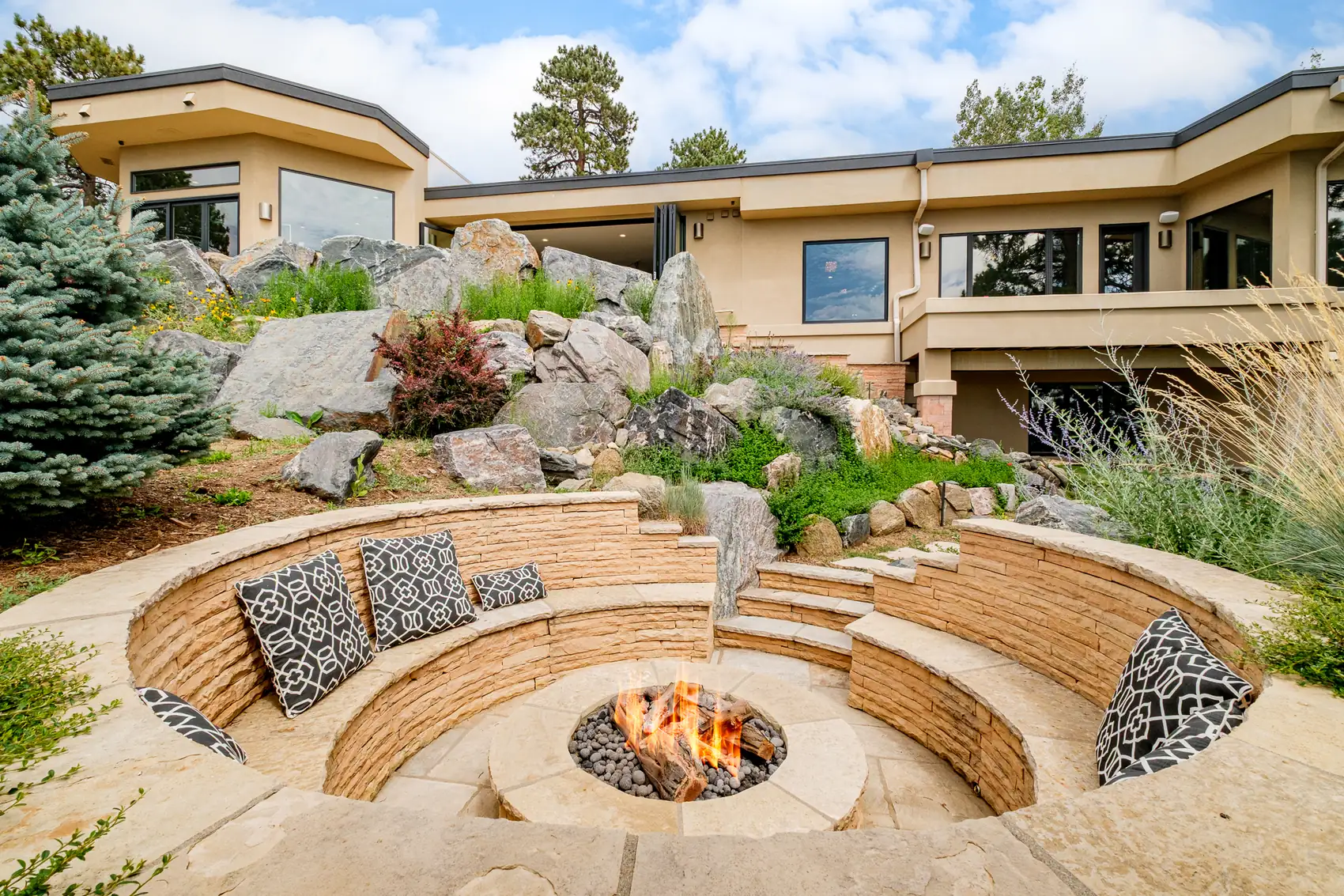 Sunken stone fire pit ringed by a curved bench beneath the rock garden.