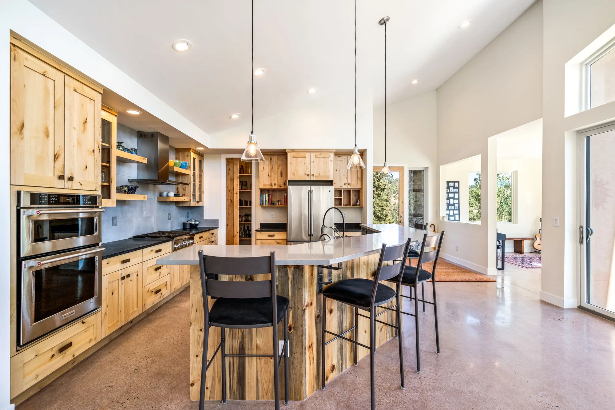 Kitchen with knotty alder cabinetry, concrete-look tile backsplash, double ovens, and a walk-in pantry