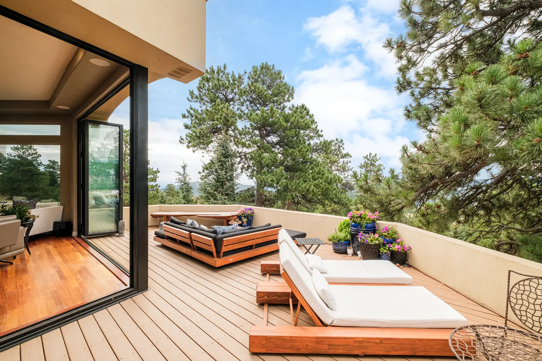 Deck seen through a fully opened sliding glass wall, with lounge seating and pines beyond.