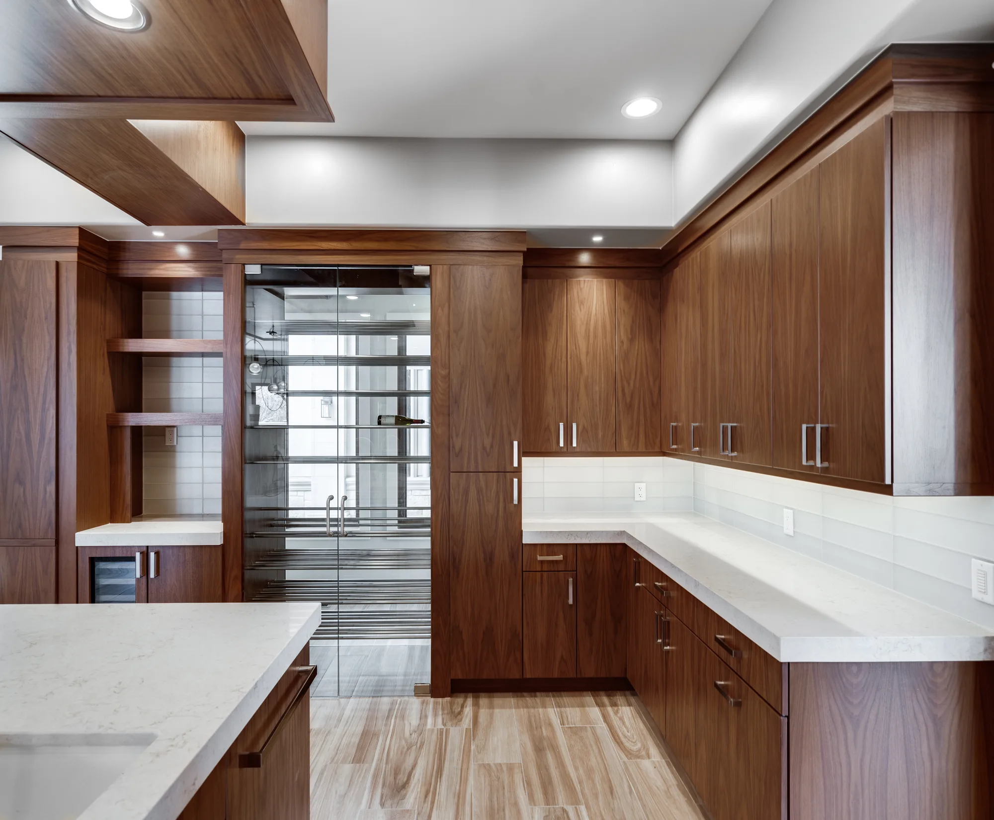 Butler's pantry in walnut with quartz counters, leading through a glass door to the wine room beyond