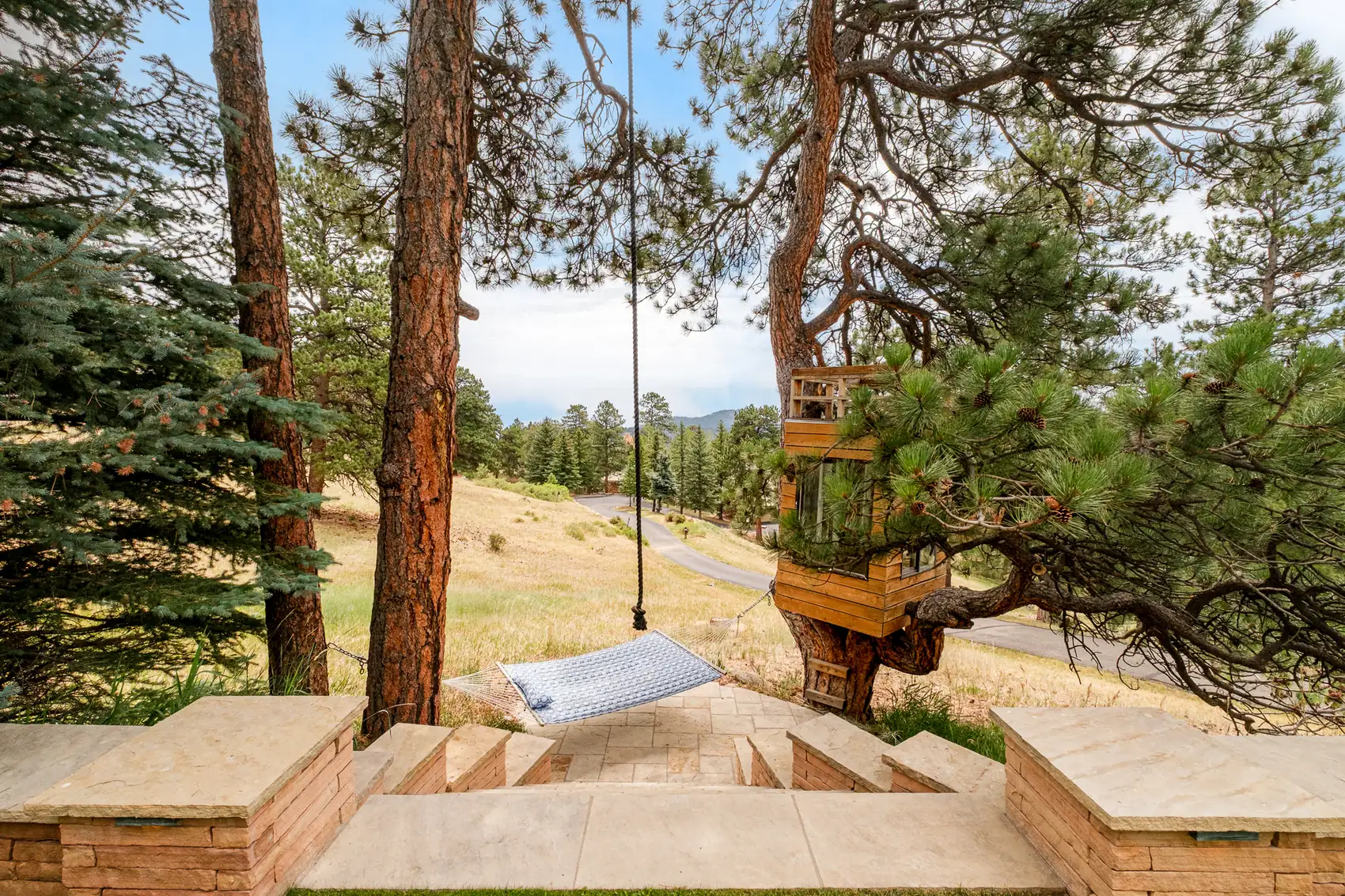 Hammock strung between ponderosas above a stone stair and open meadow.