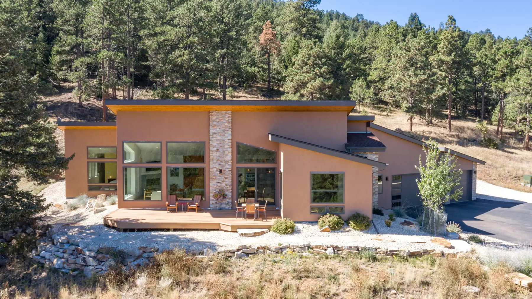 Rear elevation showing the opposing roof planes, the stone column, and the deck stepping down to the hillside