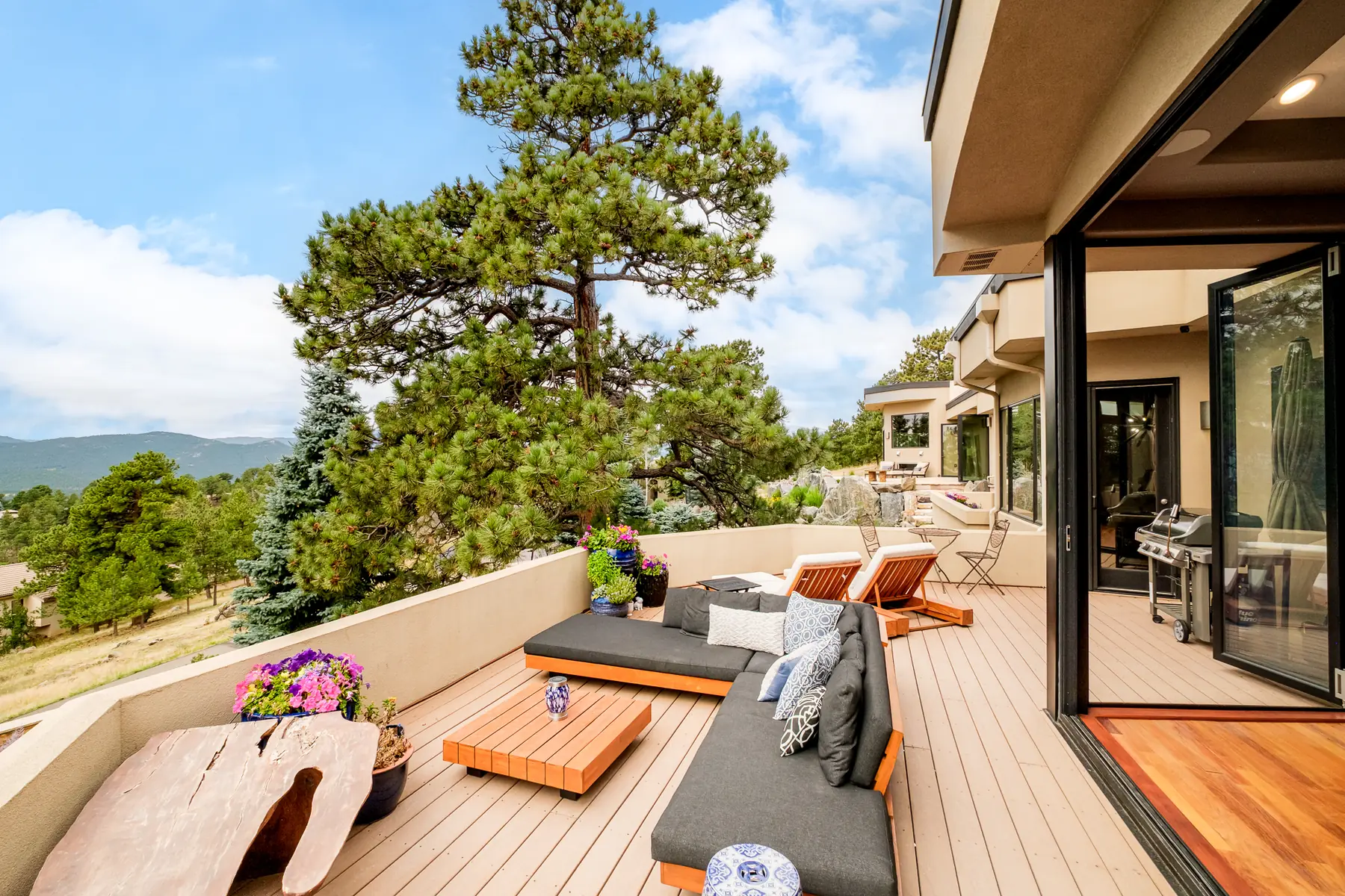 Deck running along the house with sectional seating, planters and a distant ridge.