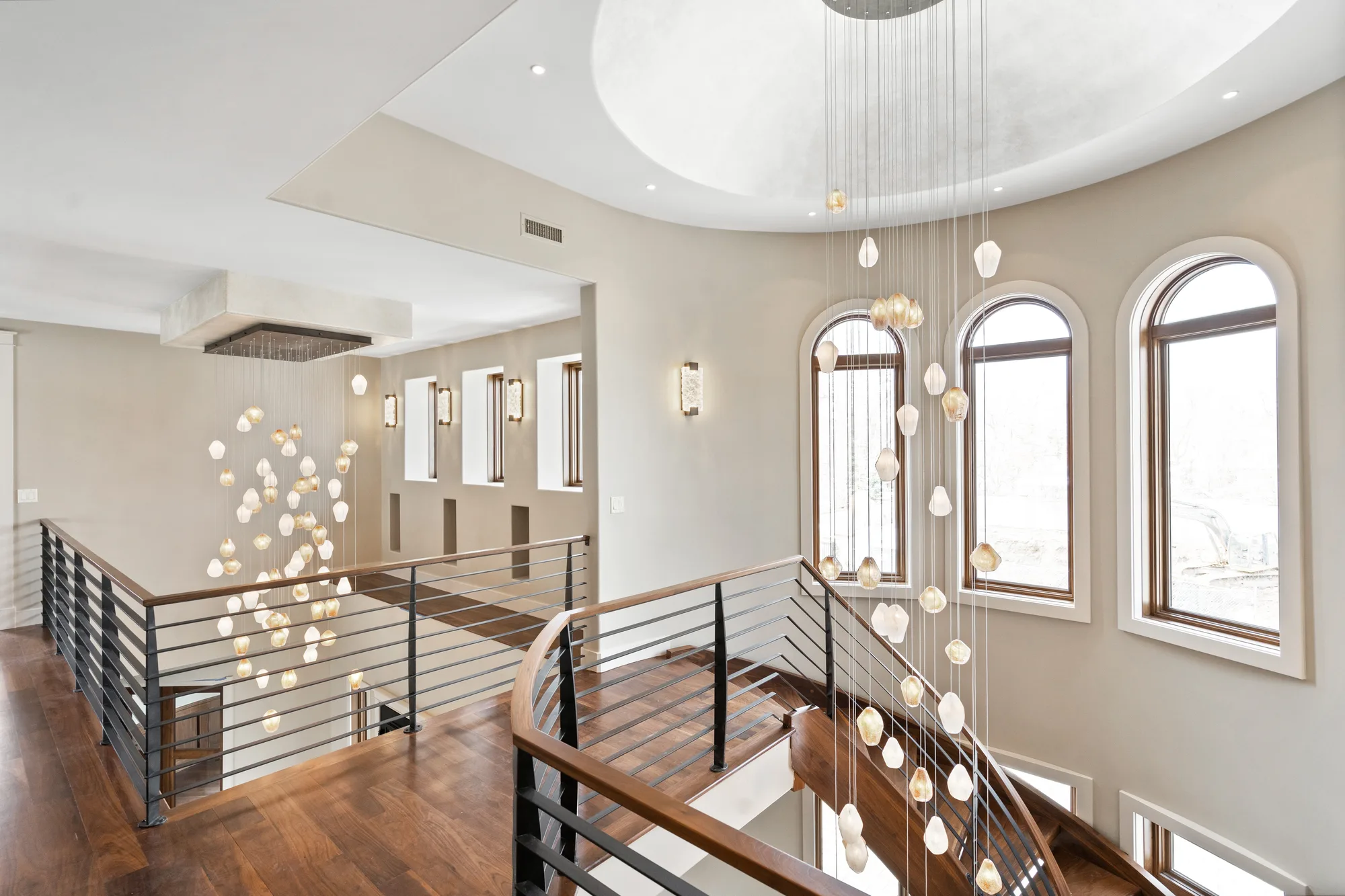 Upper landing with walnut floors and a steel rail, open to the stair volume, arched windows beyond