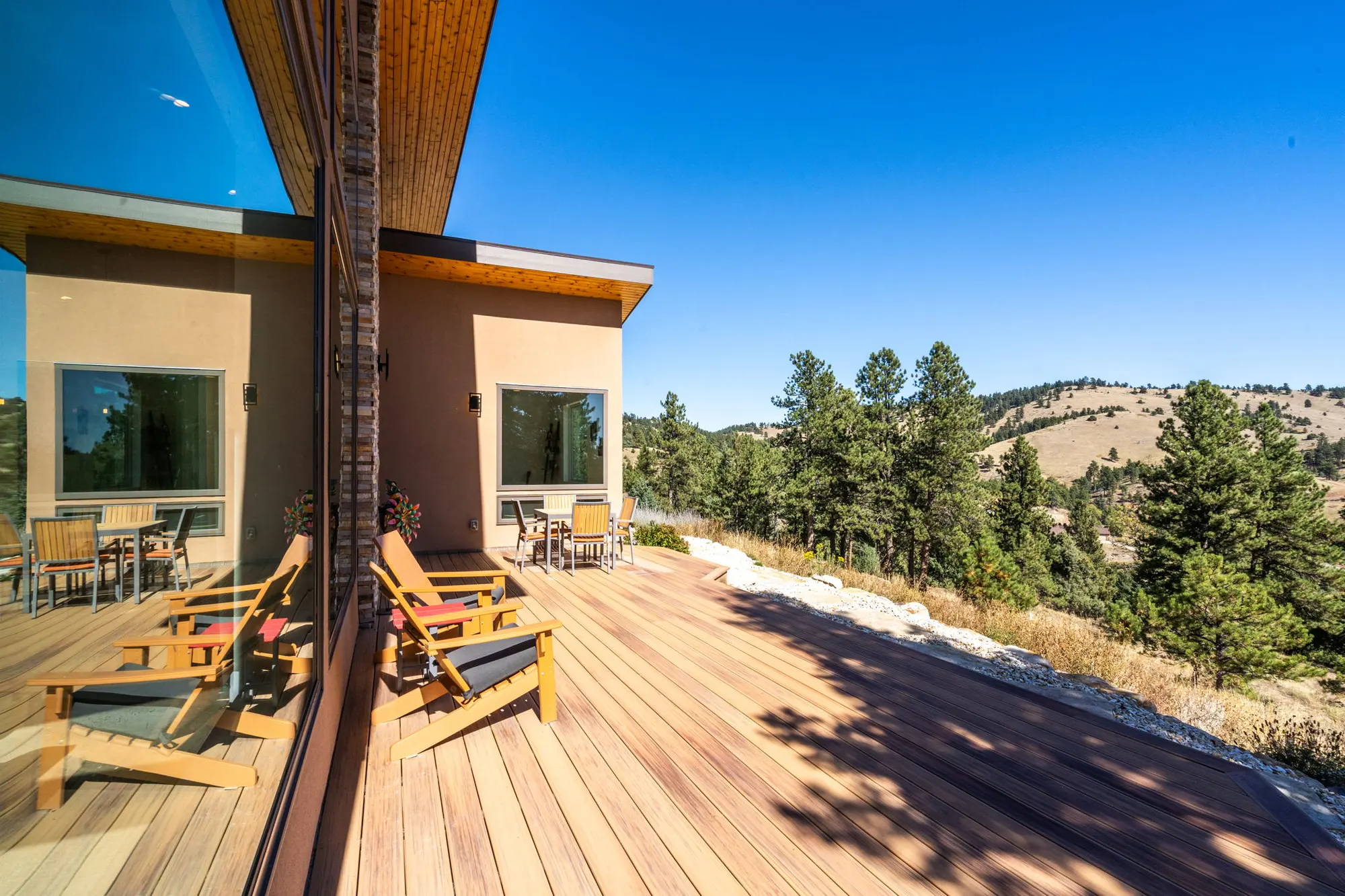 Ipe deck running along the south face of the house, with Adirondack chairs and a dining table above the canyon