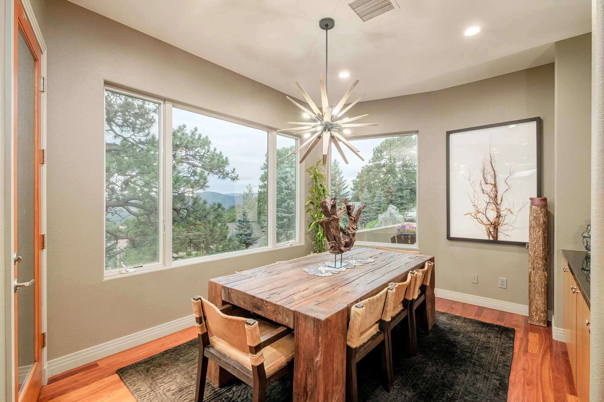 Breakfast nook with a reclaimed timber table, hide chairs and windows onto the pines.