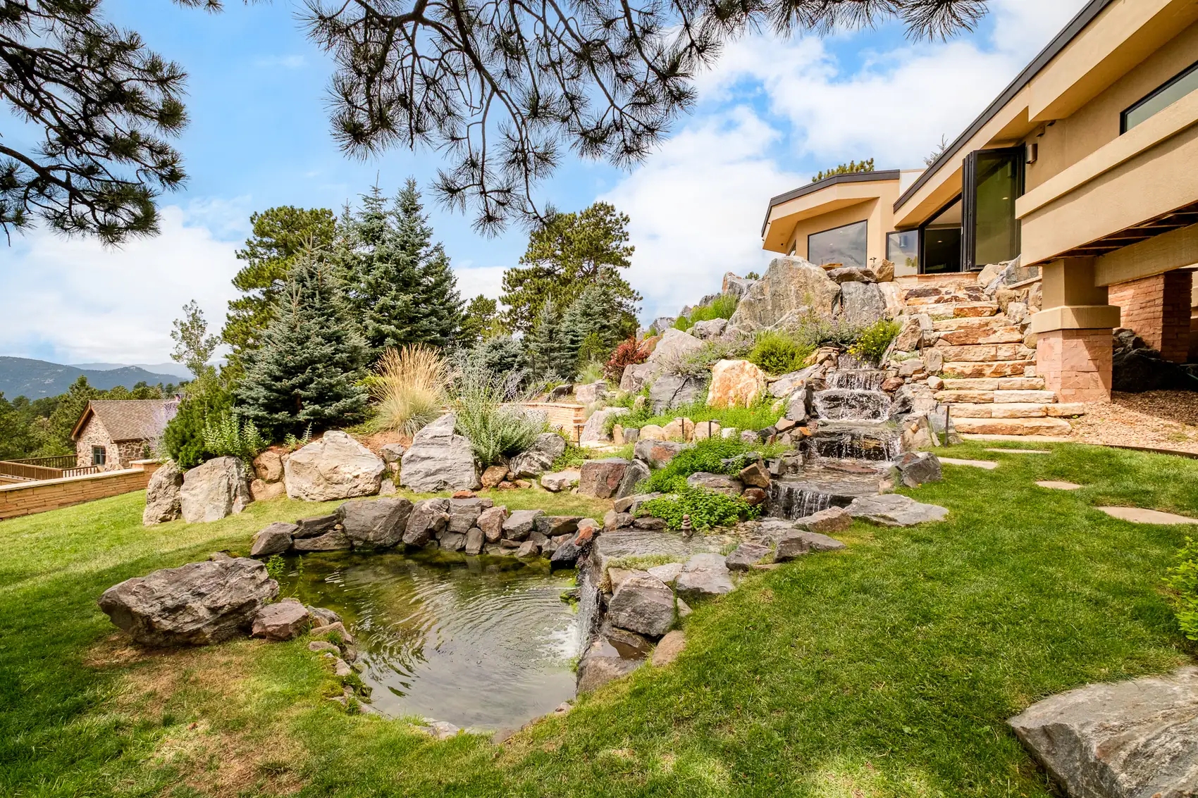 Waterfall spilling over granite boulders into a pond below the terraced house.