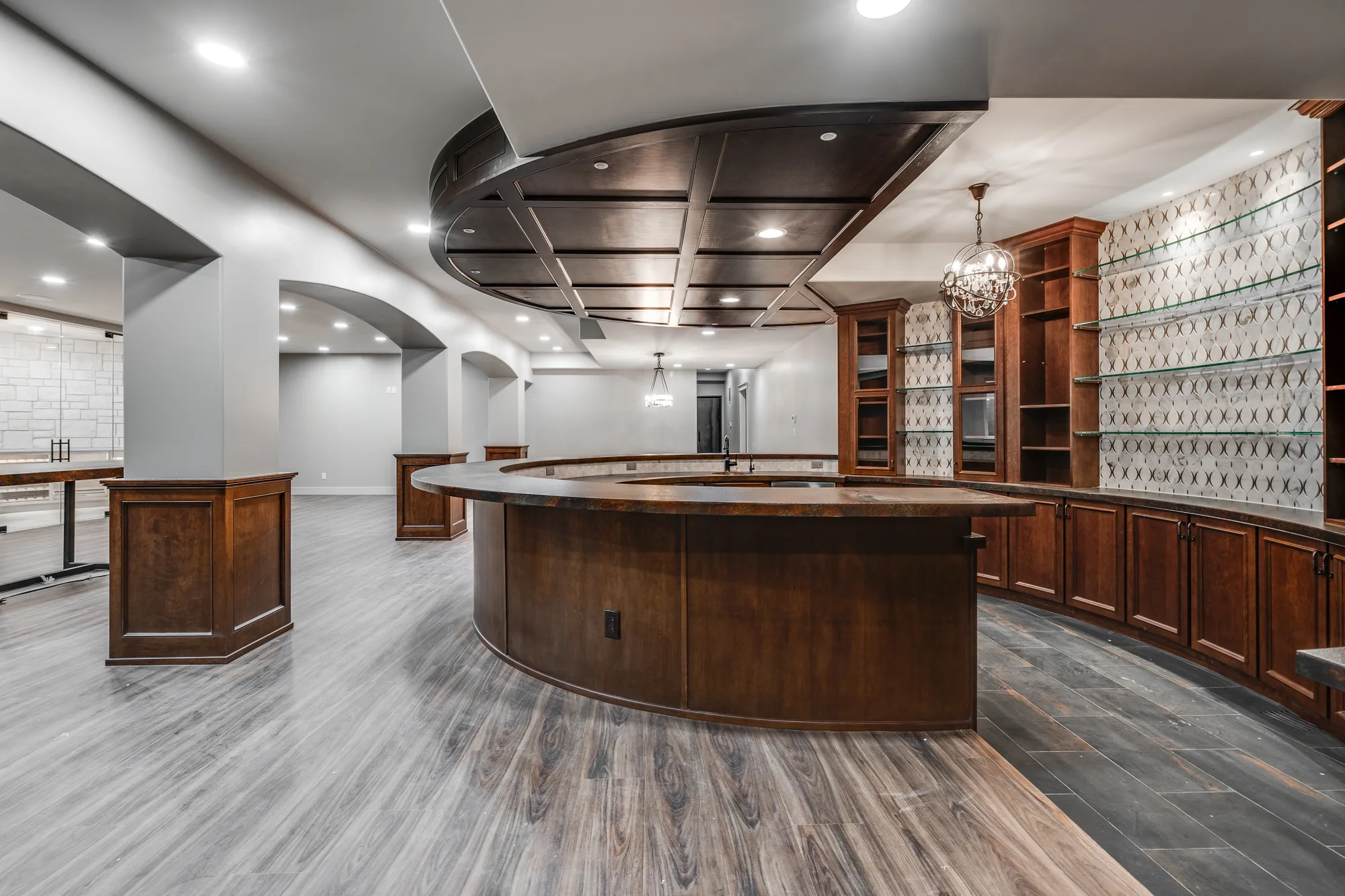 Lower level bar with a curved wood counter, a coffered wood ceiling medallion above it, and a patterned tile back wall