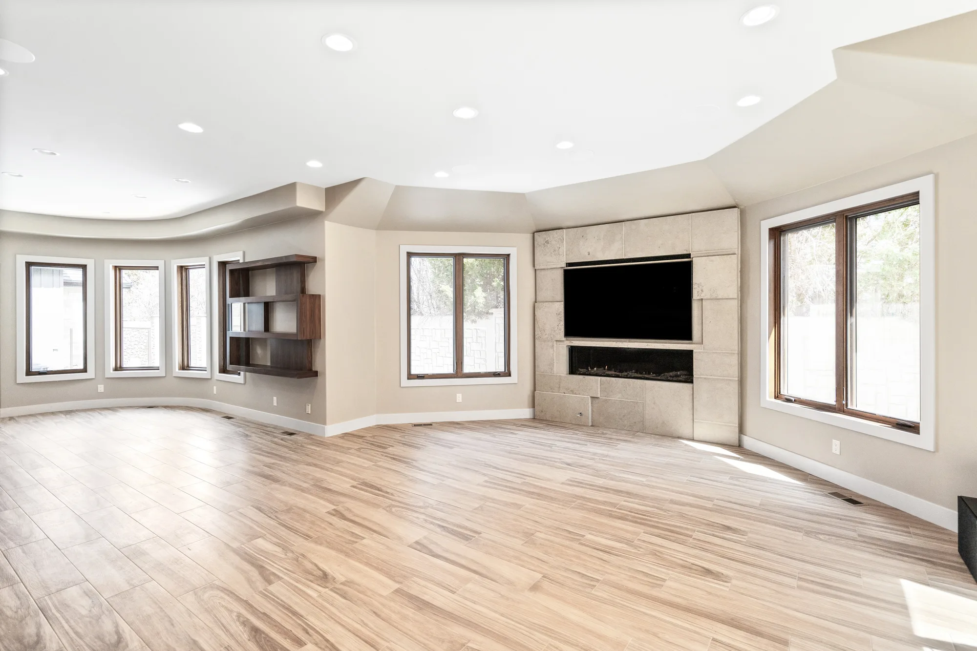 Great room with a curved wall of windows, a linear fireplace in cut limestone, and floating walnut shelves