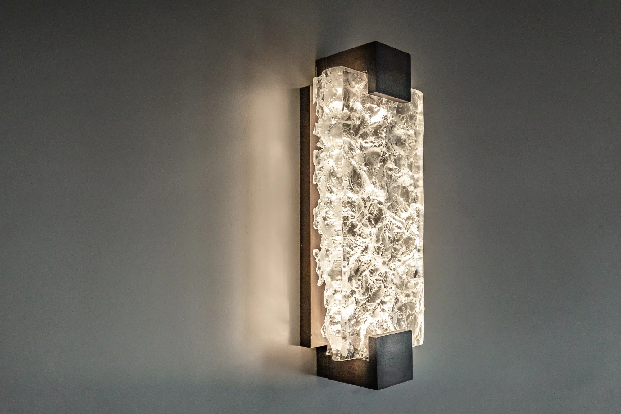 Wall sconce of cast rock crystal in a bronze frame, lit from within