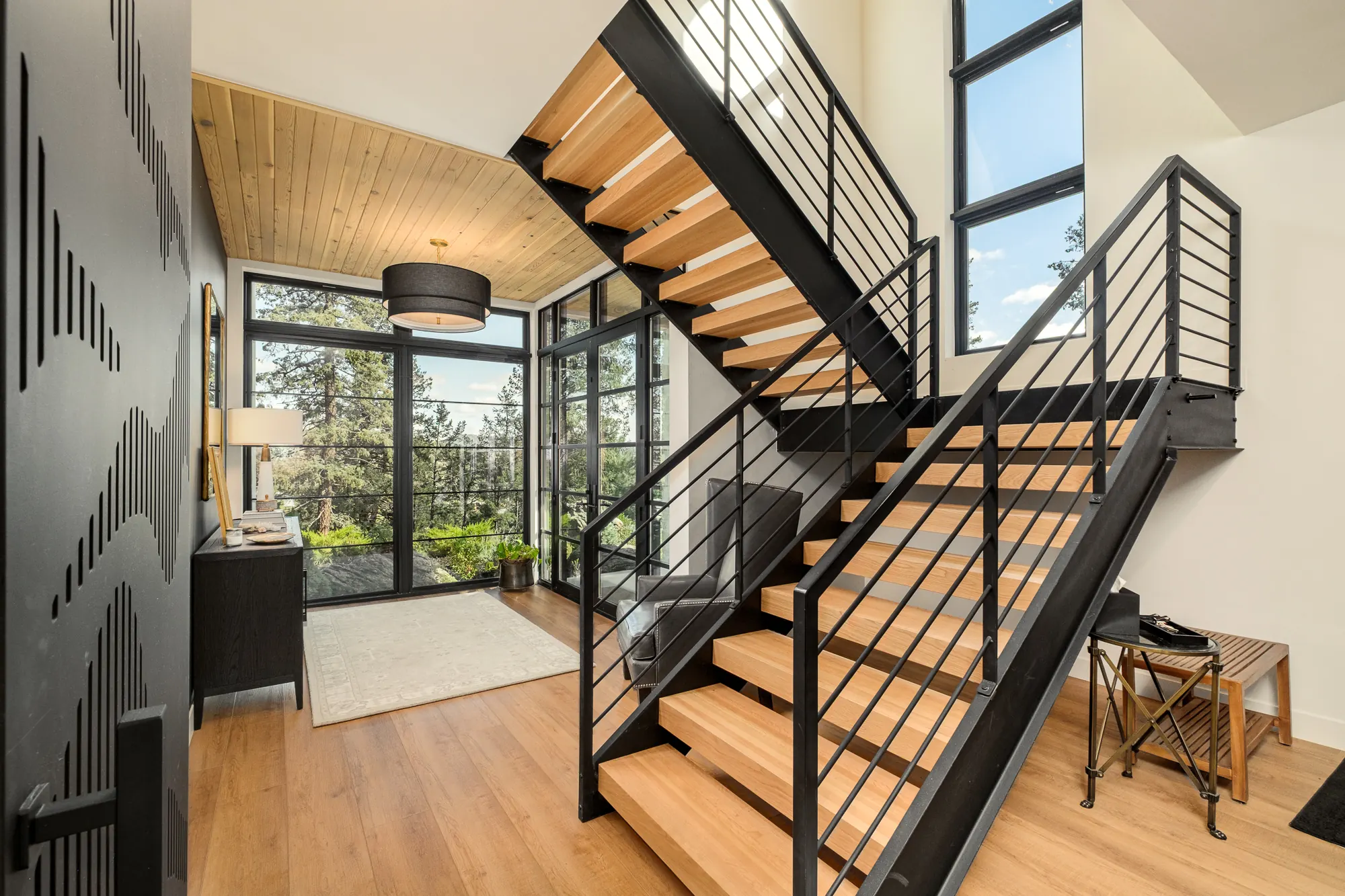 Wide view of the stair hall where oak treads, black steel railings and wood-planked ceilings intersect.