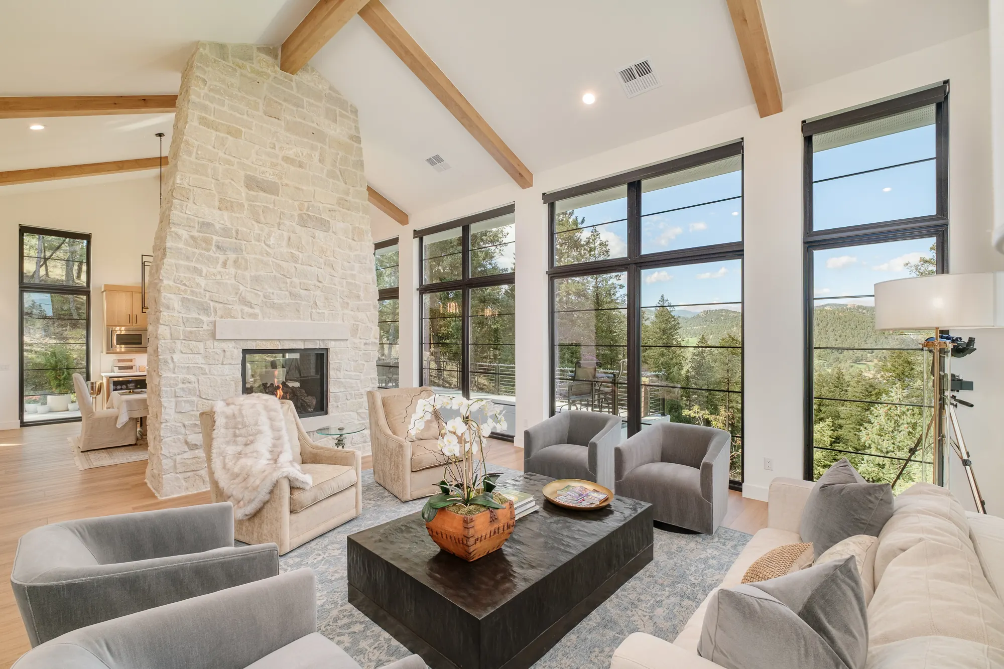 Great room with vaulted ceilings and oak beams, a floor-to-ceiling stone chimney and glass walls open to the mountain valley.
