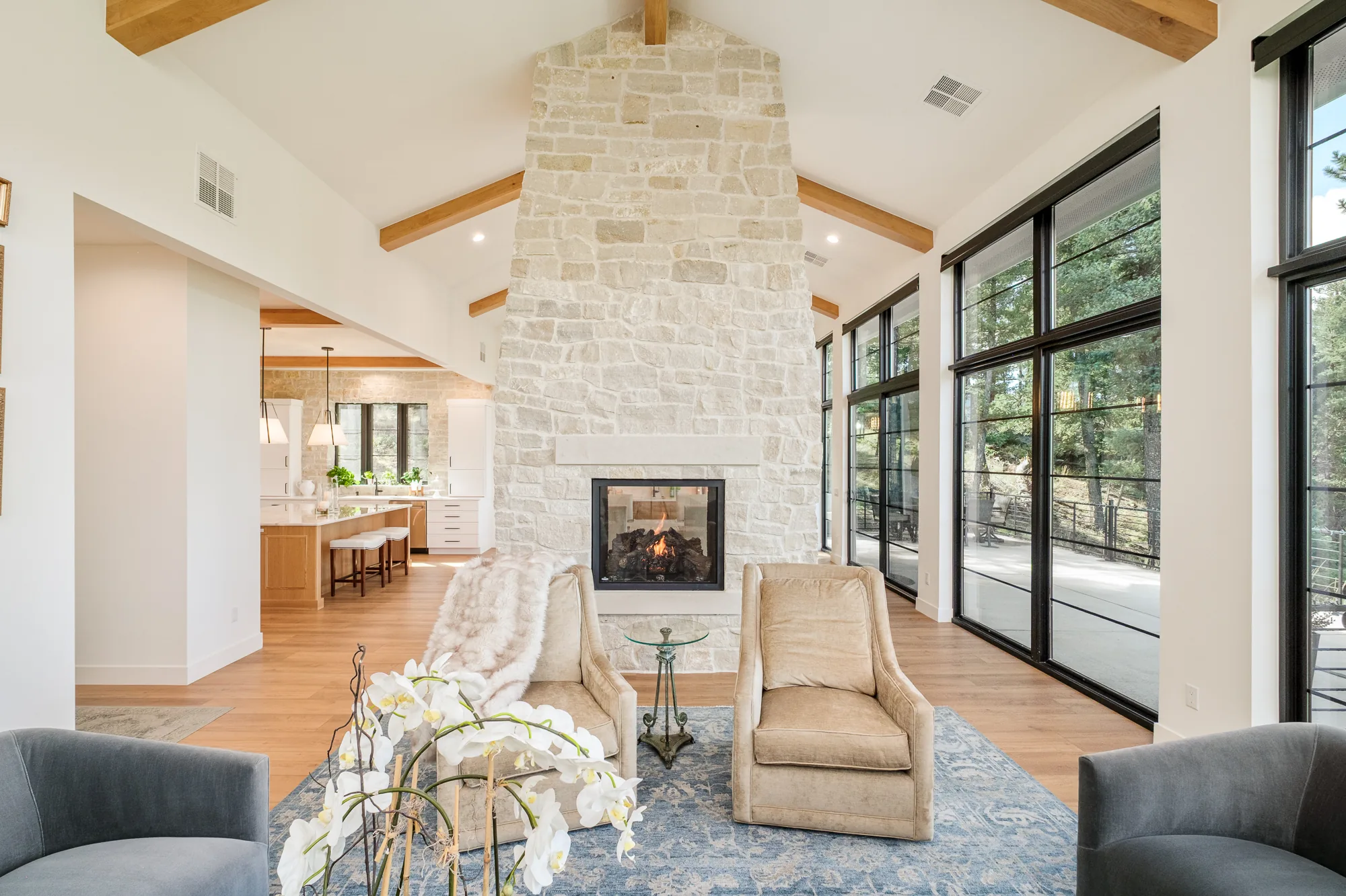 Great room fireplace framed symmetrically by light armchairs, looking through to the kitchen beyond.