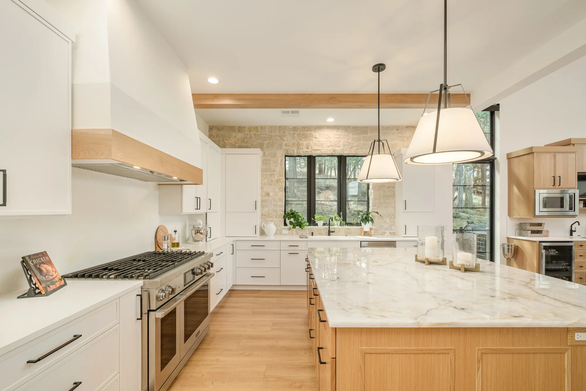 Kitchen from the range wall, showing the oak-banded plaster hood, professional range and the veined marble island.