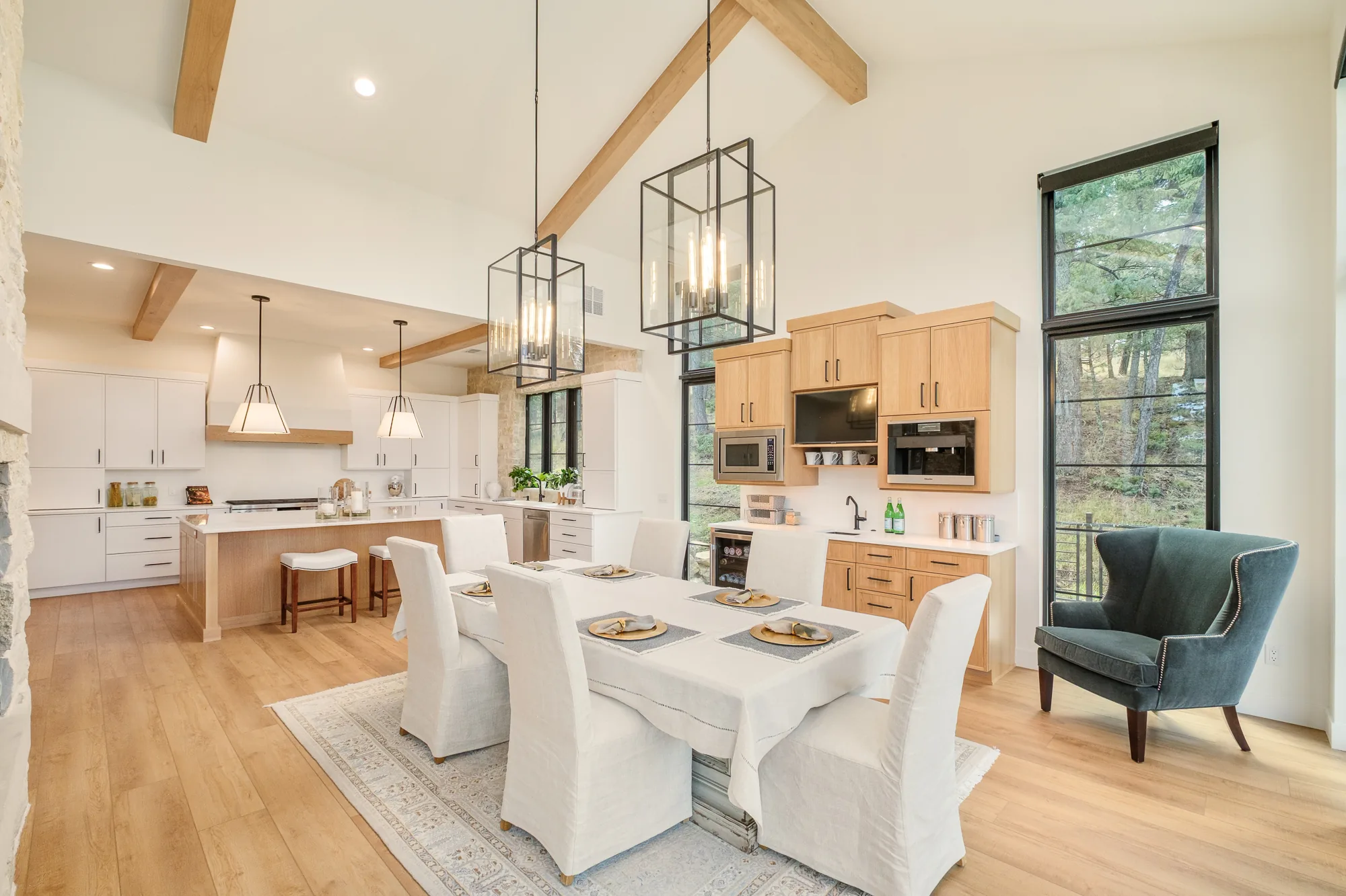 Open kitchen and dining volume under a vaulted beamed ceiling, with lantern pendants over a linen-draped table.
