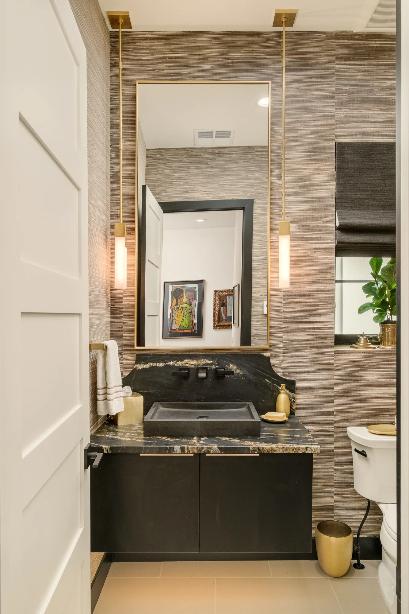 Powder room in grasscloth with a black granite slab backsplash, stone vessel sink and slender brass pendants.