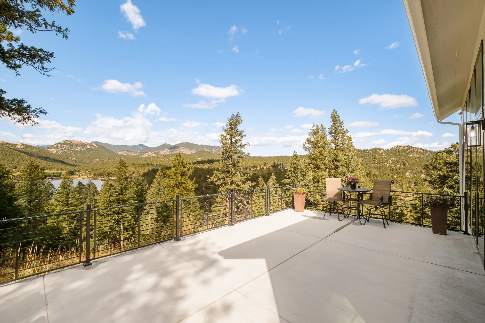 Broad concrete deck with cable railing looking out over pines, a lake and the foothills range.