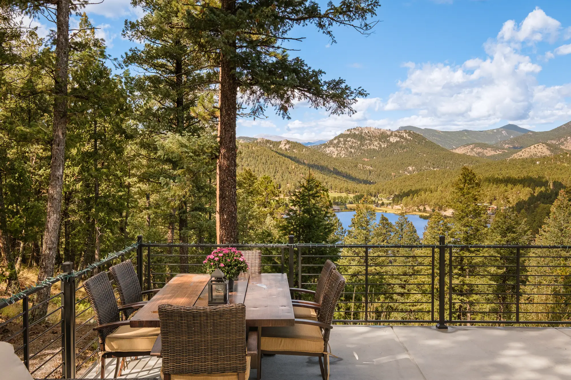 Outdoor dining table on the deck beneath tall ponderosa pines, with the lake and forested ridges beyond.
