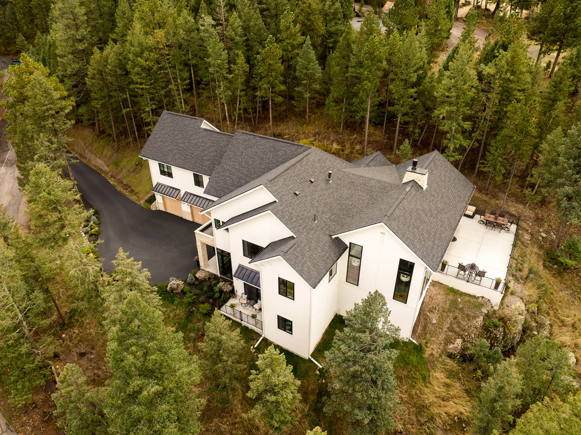 Overhead aerial of the white house and its roofline, drive and terrace set into dense pine forest.