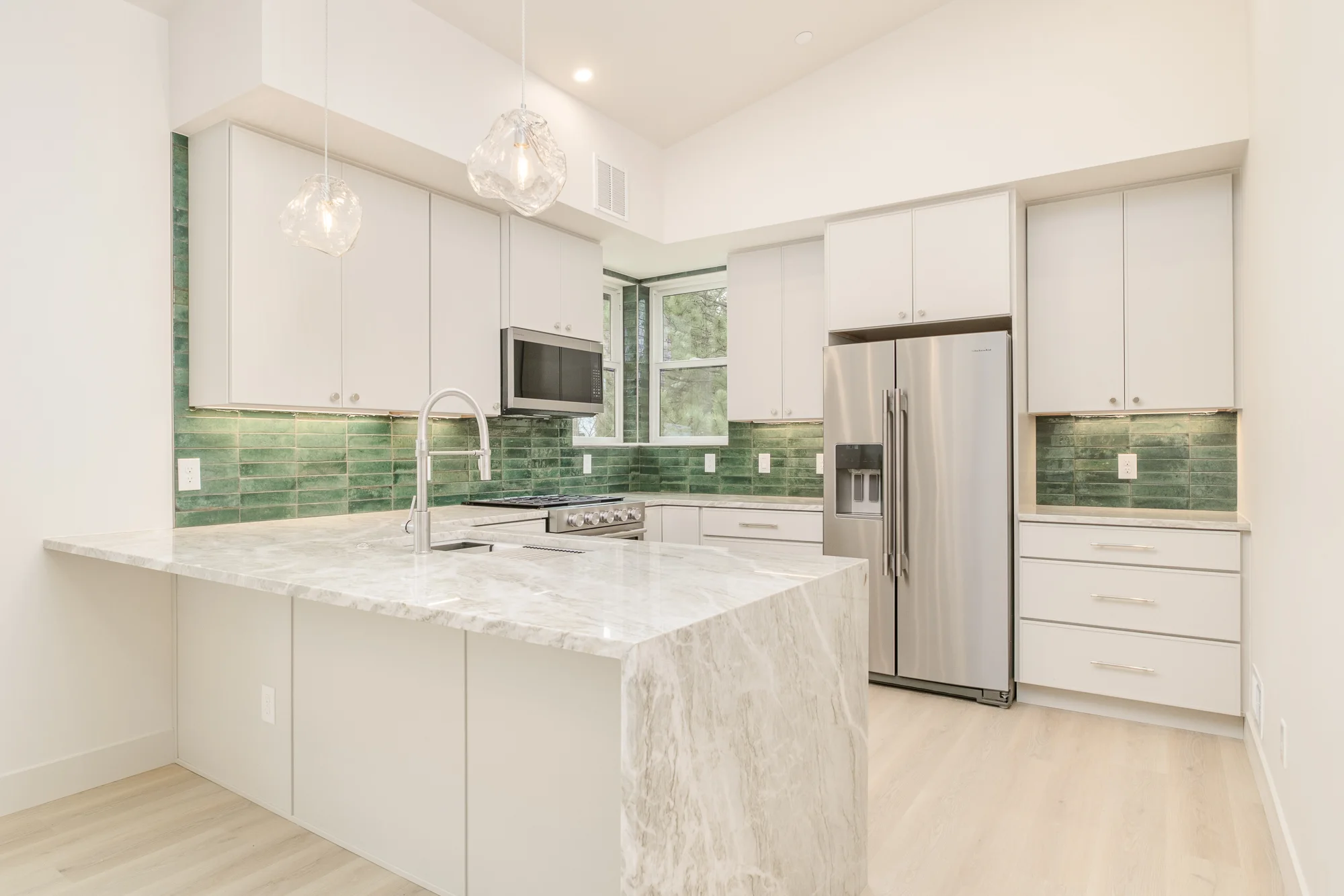 Kitchen with white cabinetry, green glazed tile backsplash, and a quartzite peninsula with a waterfall end