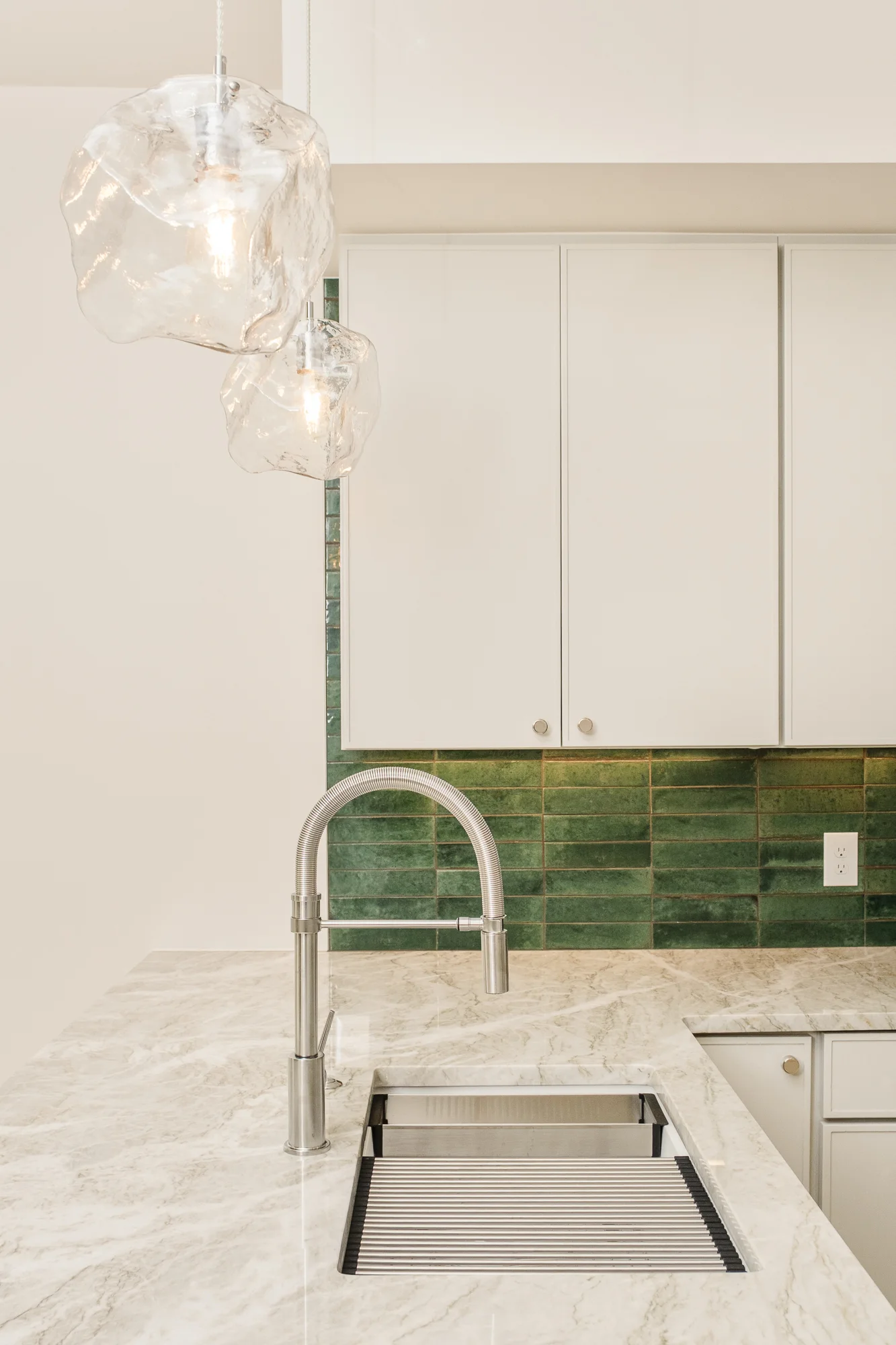 Two hand-blown glass pendants above the sink against a green glazed tile backsplash