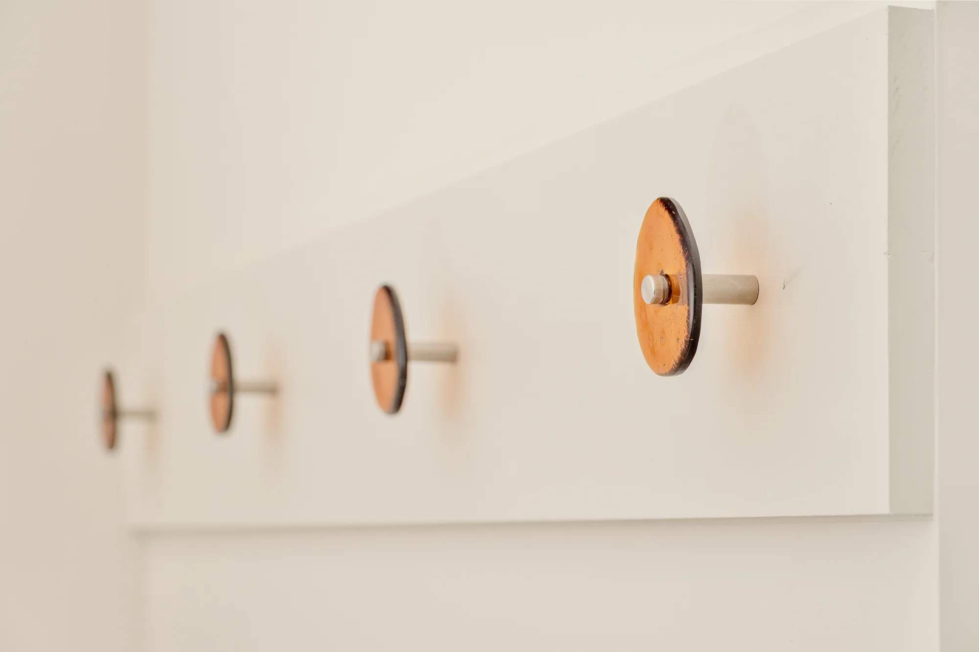 A row of amber cast-glass coat hooks on brushed steel posts along a white rail