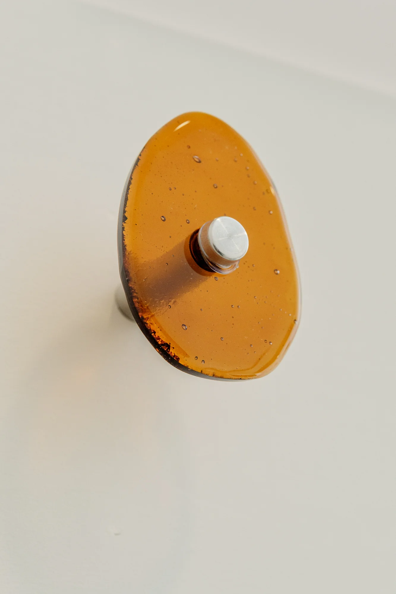Close detail of a single amber cast-glass coat hook on a brushed steel post