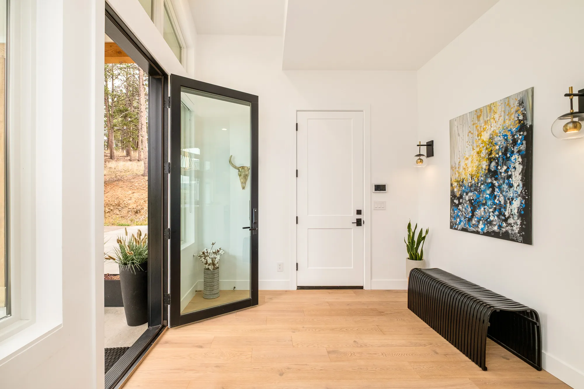 Black steel-framed glass front door opening into a bright white entry