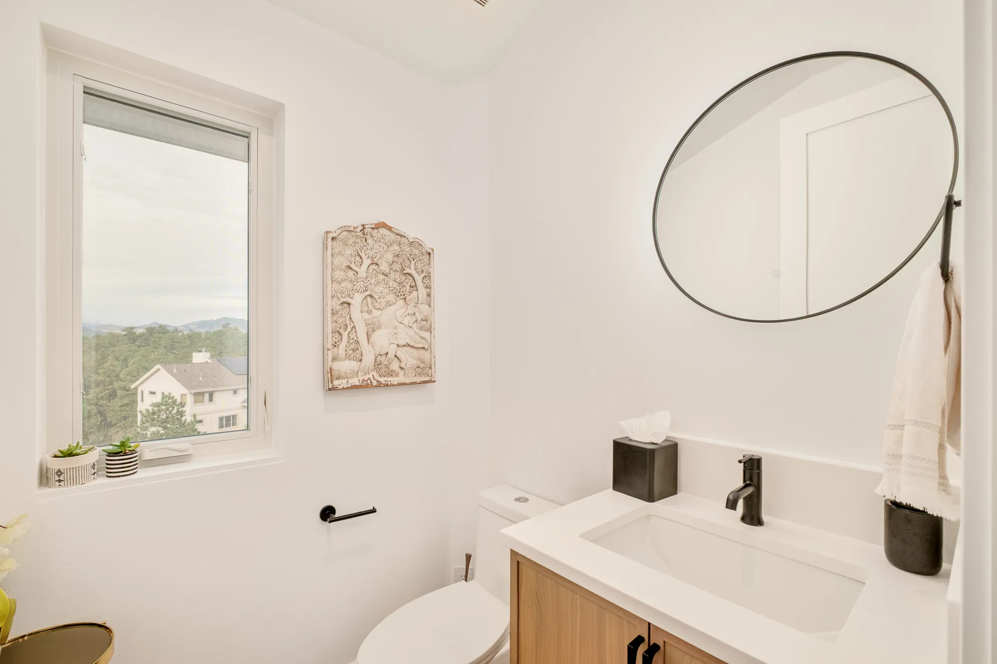 Powder room with a round black mirror, wood vanity and a window to the trees