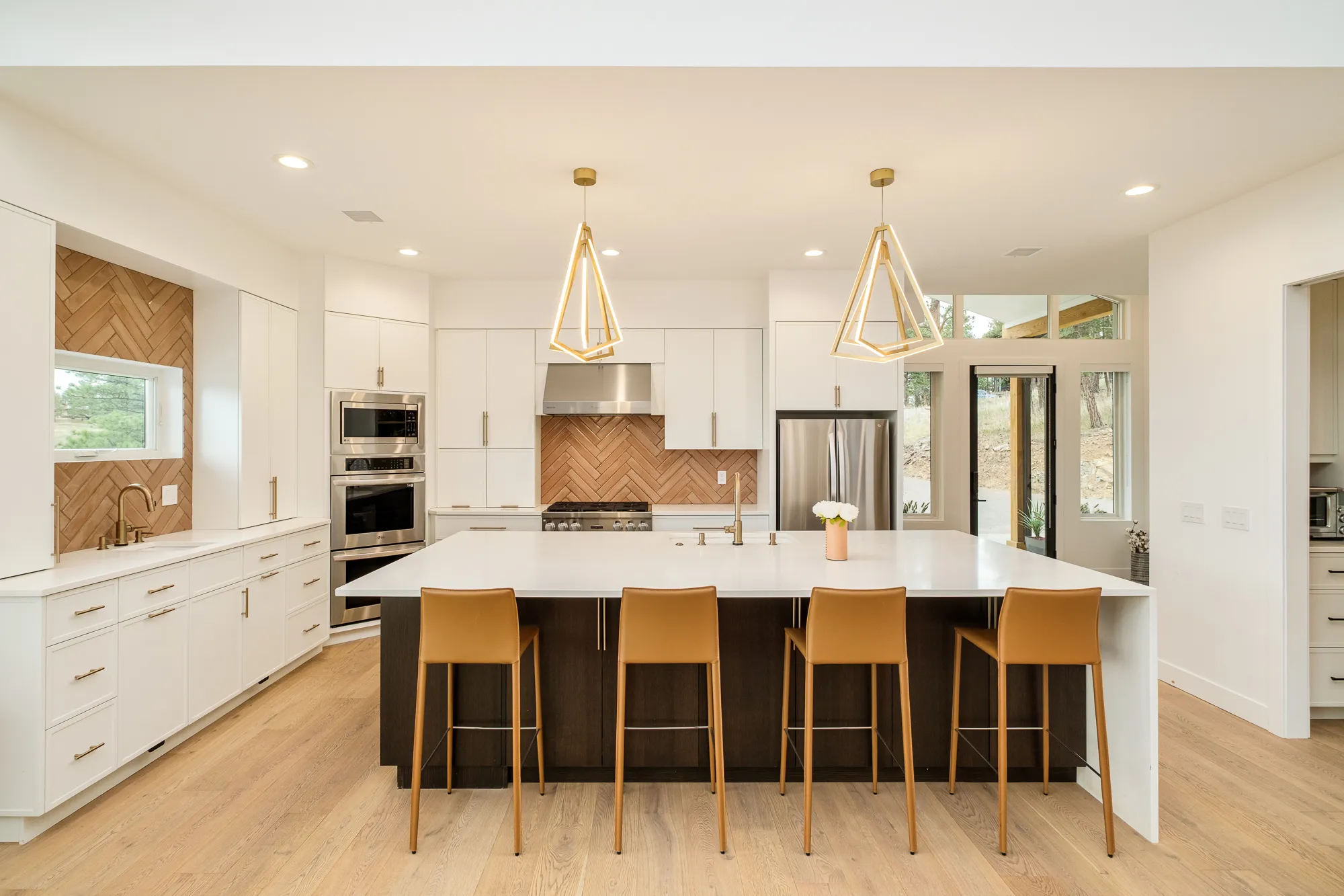 Kitchen island with leather counter stools beneath brass pendant lights