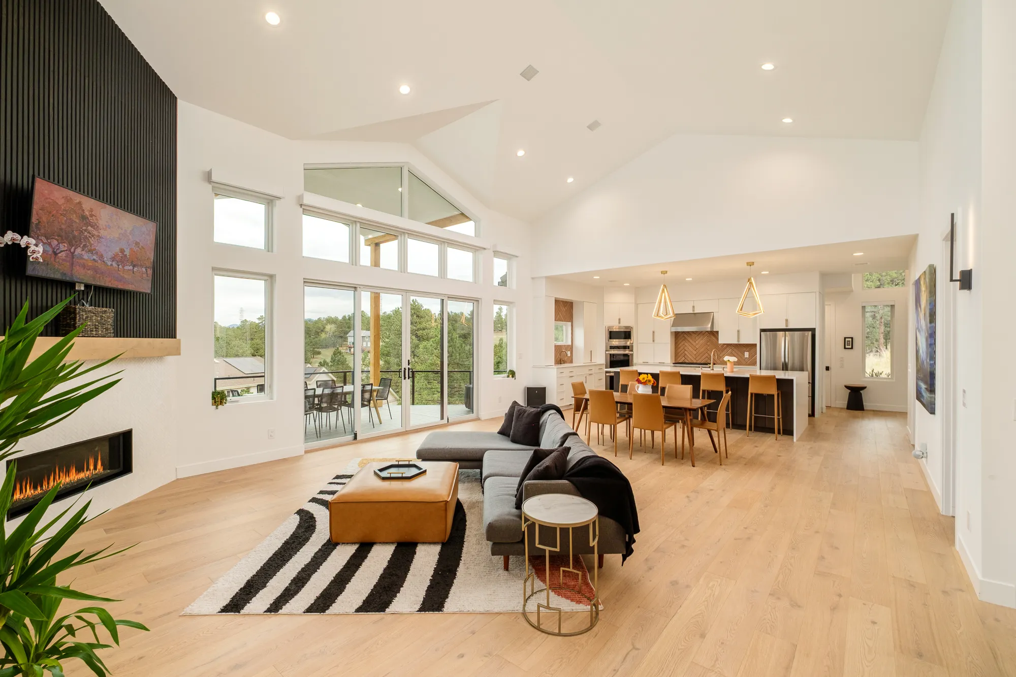 Living room with a striped rug, sectional and floor-to-ceiling windows to the forest