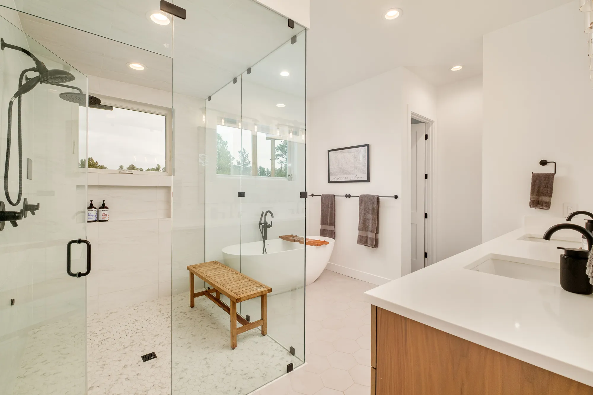Glass-enclosed walk-in shower with a teak bench and black fixtures