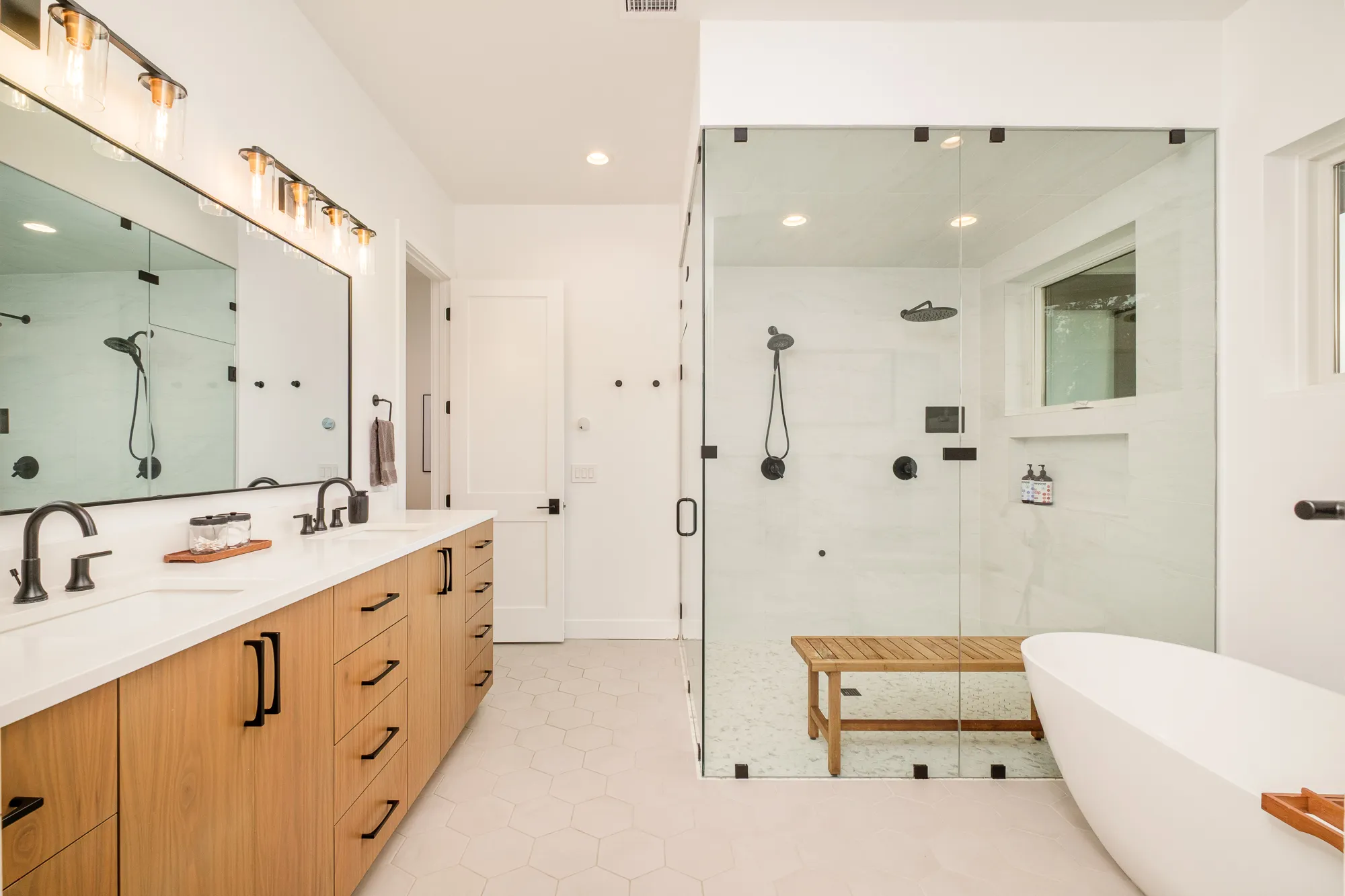 Primary bath with a long wood vanity, freestanding tub and glass shower