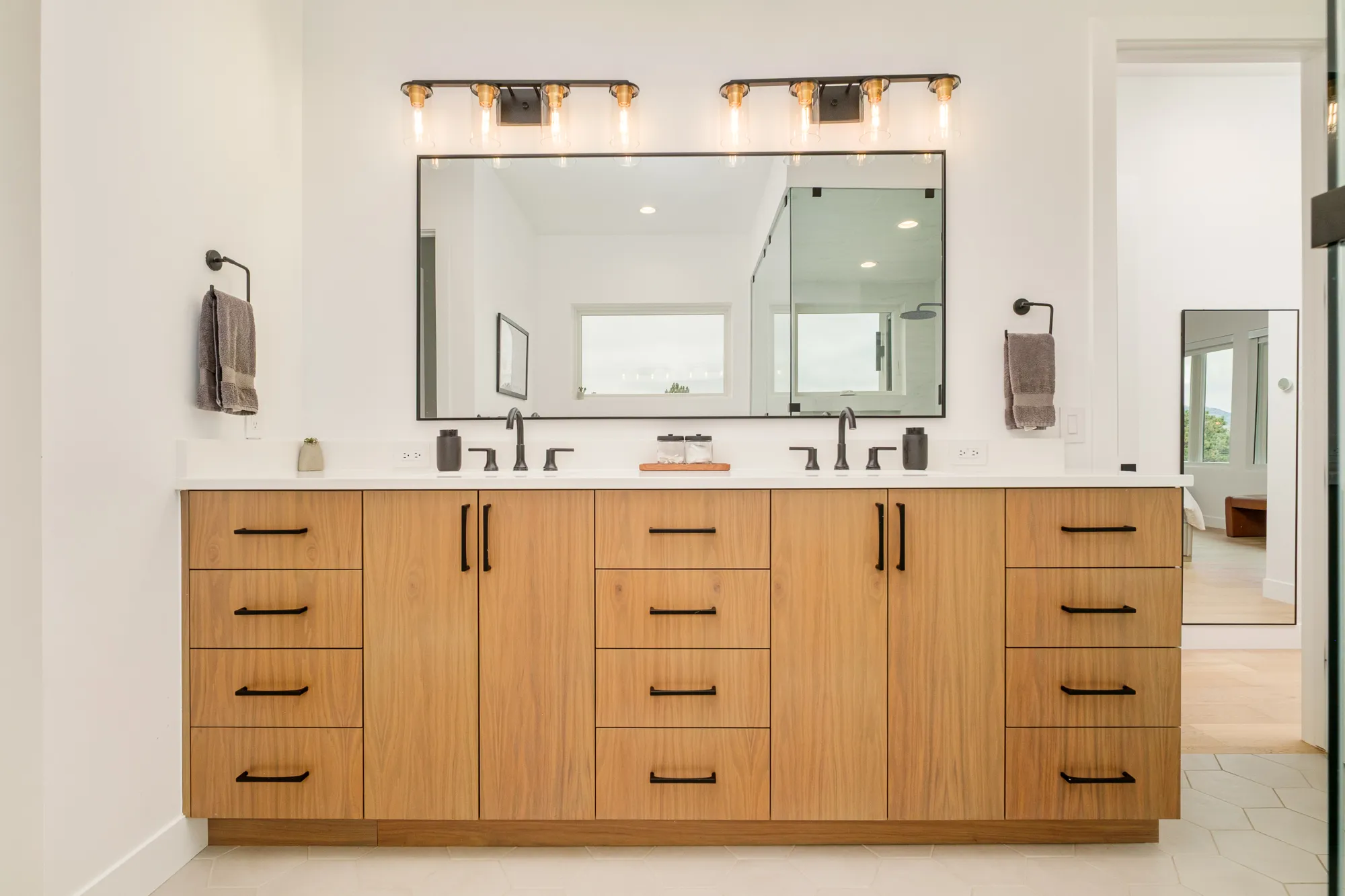 Double wood vanity with black hardware beneath brass sconces