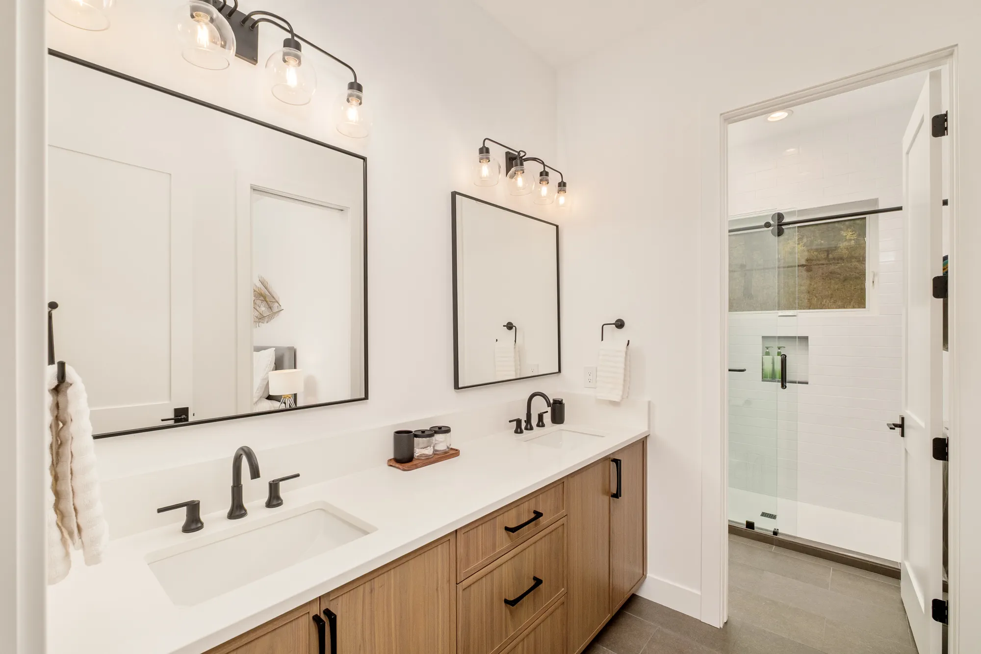 Bath with a wood vanity, black fixtures and a glass shower